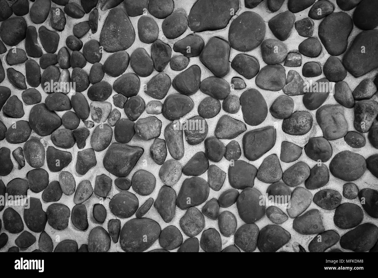 Eine schwarze und weiße Nahaufnahme von einer Wand aus glatten Steinen eingebettet in Zement Mörtel gemacht Stockfoto