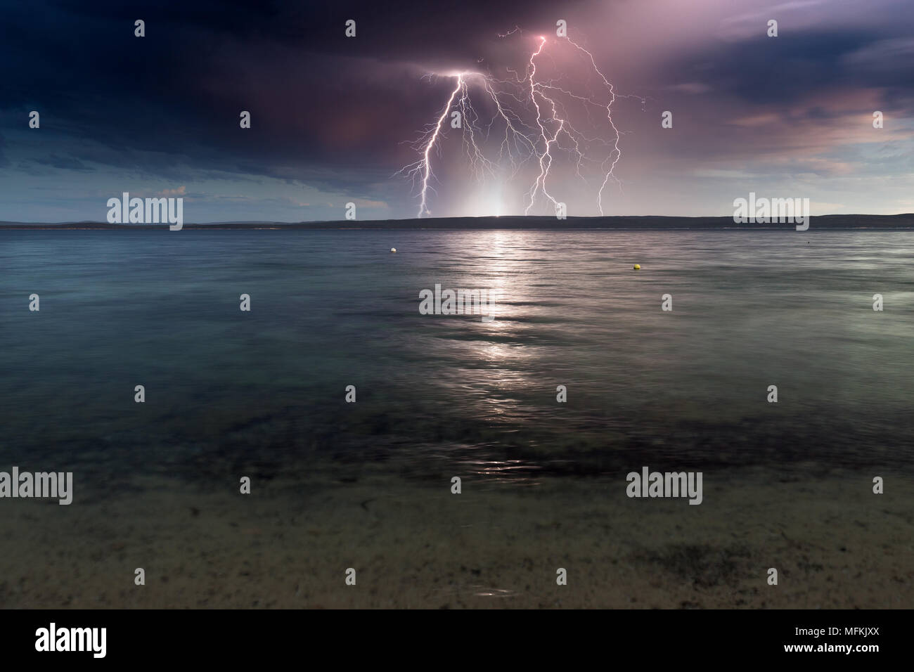 Spektakuläre Blitze über eine ruhige Ocean Bay auf ein Ominöses, dunklen, stürmischen Tag. Stockfoto