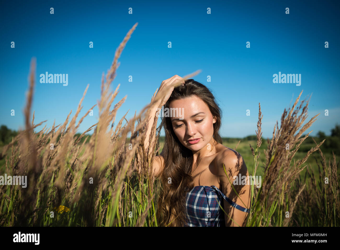 Junge hübsche Frau versteckt in einem Feld von Gras in die Landschaft. Schöne Mädchen genießt die sonnigen Tag auf dem Hintergrund der Natur. Stockfoto