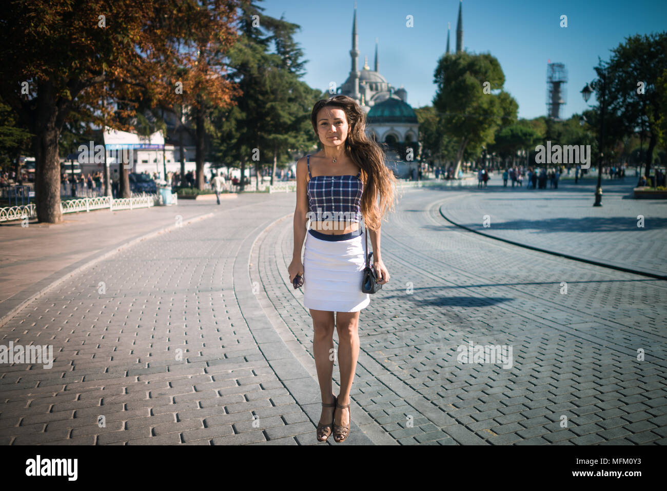 Junge lächelnde Frau springt bei Square auf dem Hintergrund der Moschee und Bäume im Sommer sonnigen Tag. Hübsches Mädchen mit langen Haaren genießt Urlaub in Istanbul Stockfoto