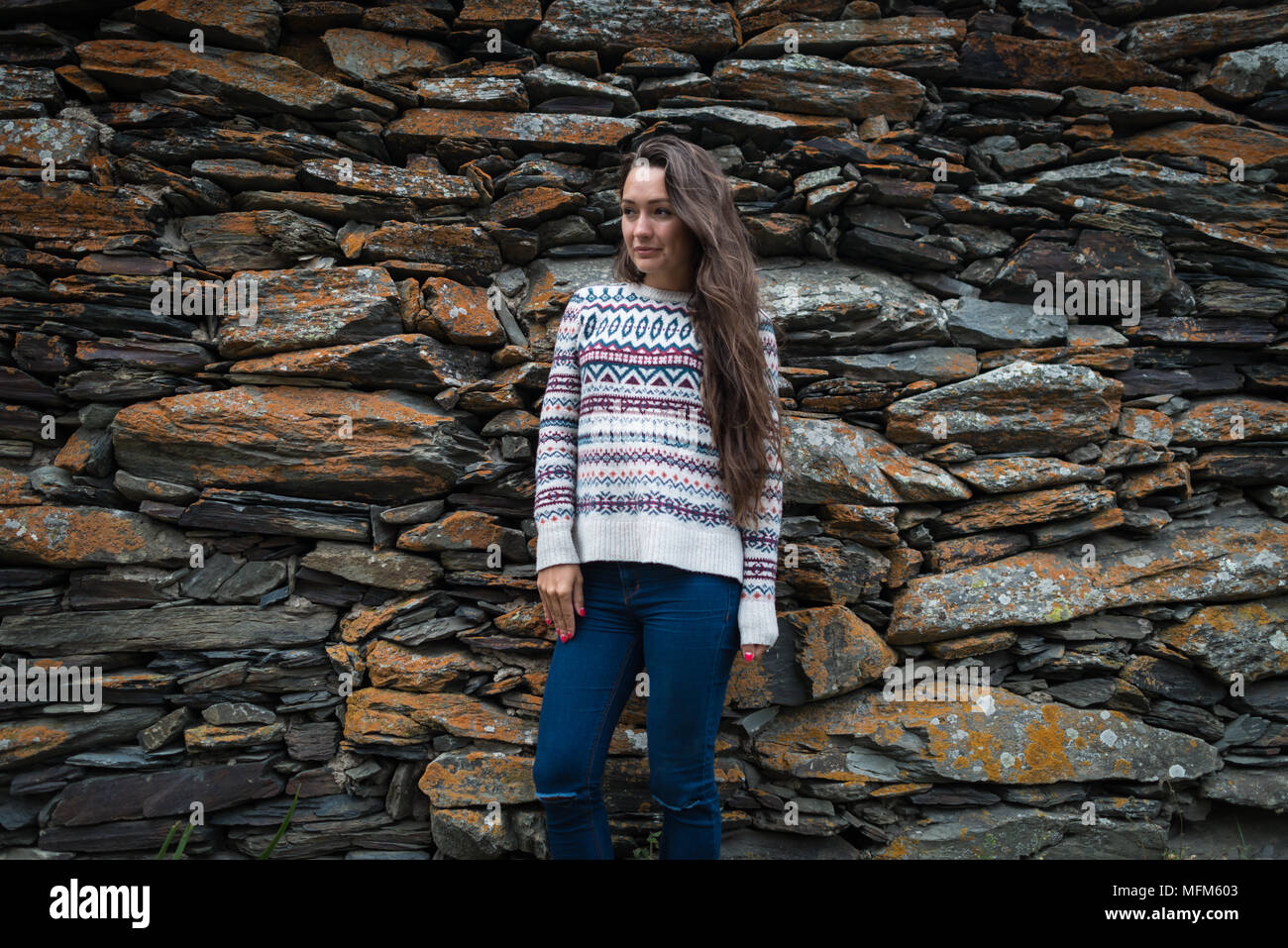 Junge Frau steht auf dem Hintergrund der Steine. Ansicht von vorne. Stilvolle Mädchen in Pullover und Jeans ist weg schauen Stockfoto