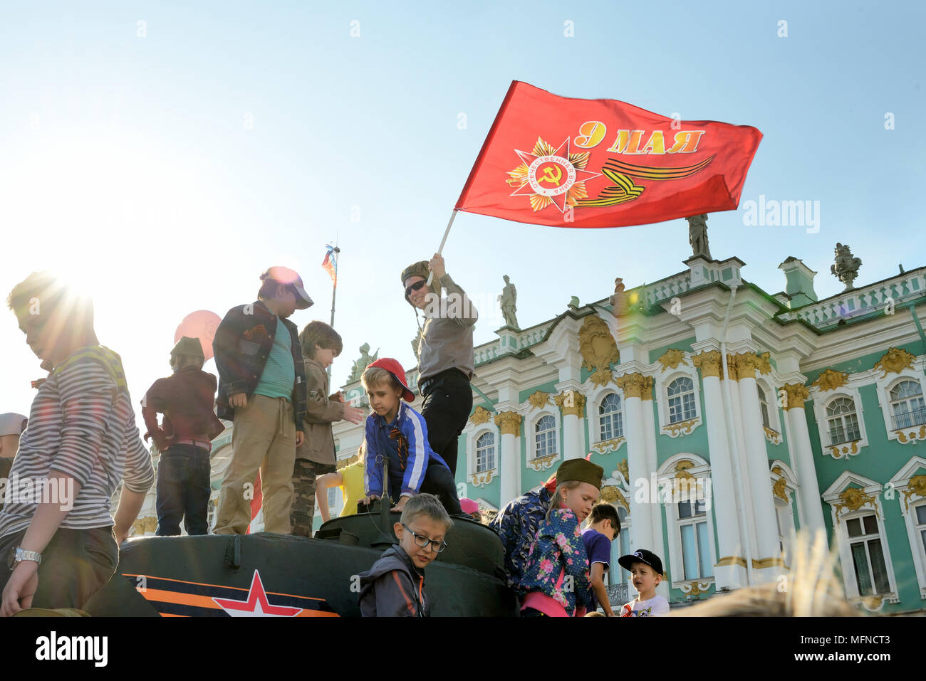 Ein Mann in einem tankman Helm hält ein Flag auf eine Bekämpfung des Fahrzeugs, die Kinder sind in der Nähe, Dvortsovaya Square, Russland Stockfoto