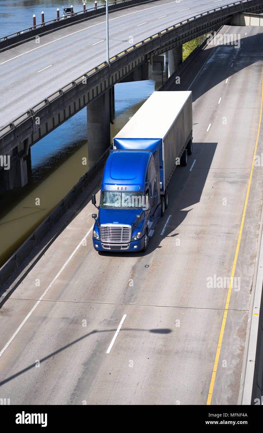 Big Rig blau American Semi Truck Transport von kommerziellen Ladung im abgedeckten Auflieger mit Spoiler unter Drehen überführung Straße Kreuzung entlang der Stockfoto