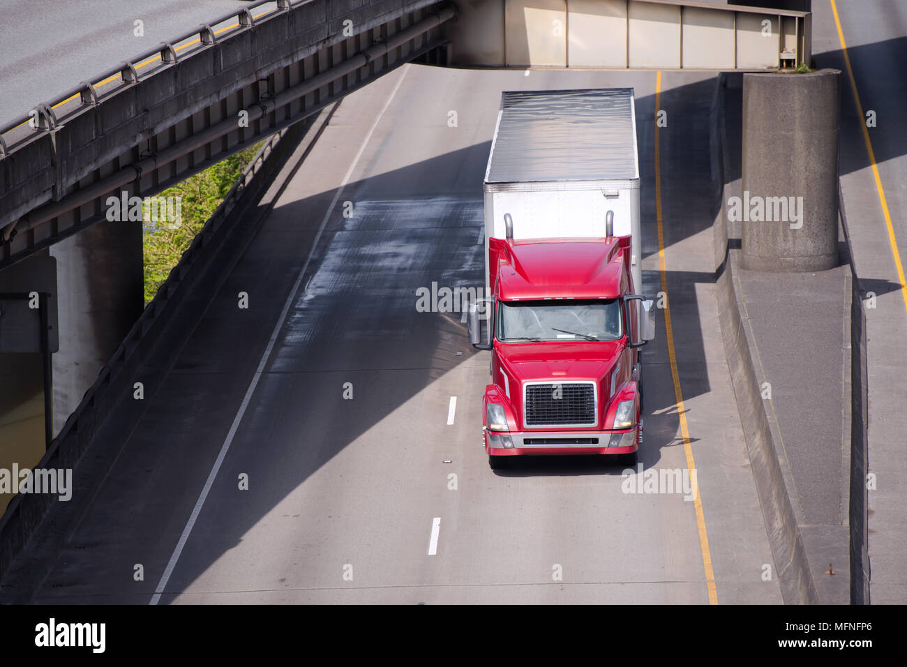 Big Rig red American Semi Truck Transport von kommerziellen Ladung trocken van Auflieger gehen unter Drehen überführung Straße Kreuzung entlang der Stockfoto