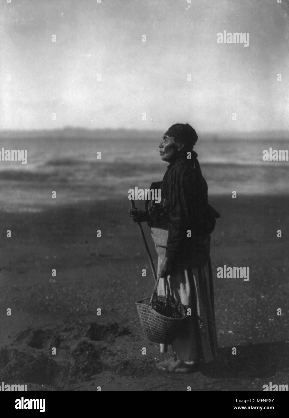 American Indian stehende Frau mit Korb am Strand, c 1910. Foto von Edward Curtis (1868-1952). Stockfoto