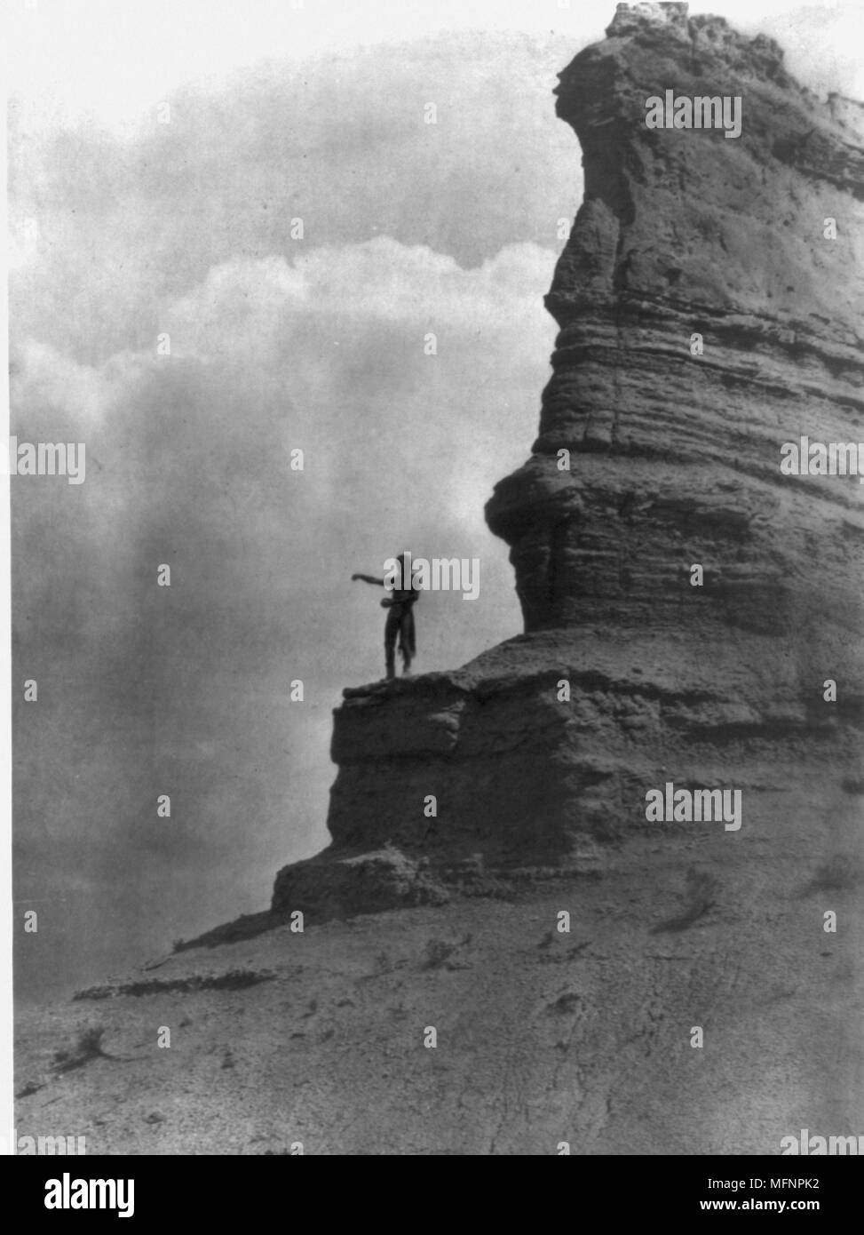 Barechested Tewa Mann, hoch auf einem Felsen, Arme vor ihm ausgebreitet, als er Maismehl streuseln als Angebot zu Beginn des Tages. Vielleicht auf der Sonne, oder einige andere Gottheit oder auf banale tägliche Ereignisse, 1927. Foto von Edward Curtis (1868-1952). Stockfoto
