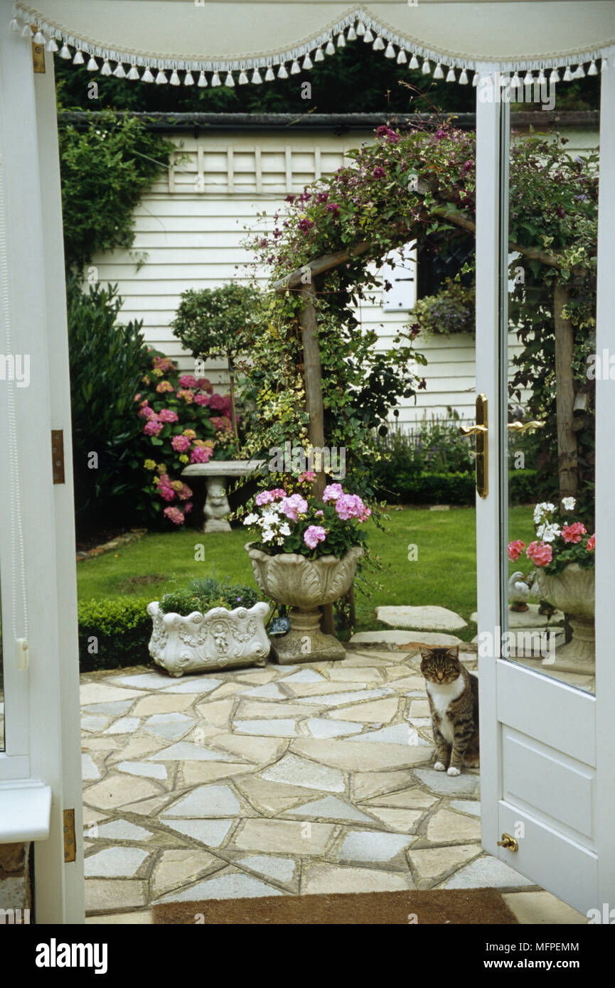 Blick durch die Tür zum Garten mit einer Terrasse vor einer kleinen Wiese mit Stein Blumentöpfe. Stockfoto