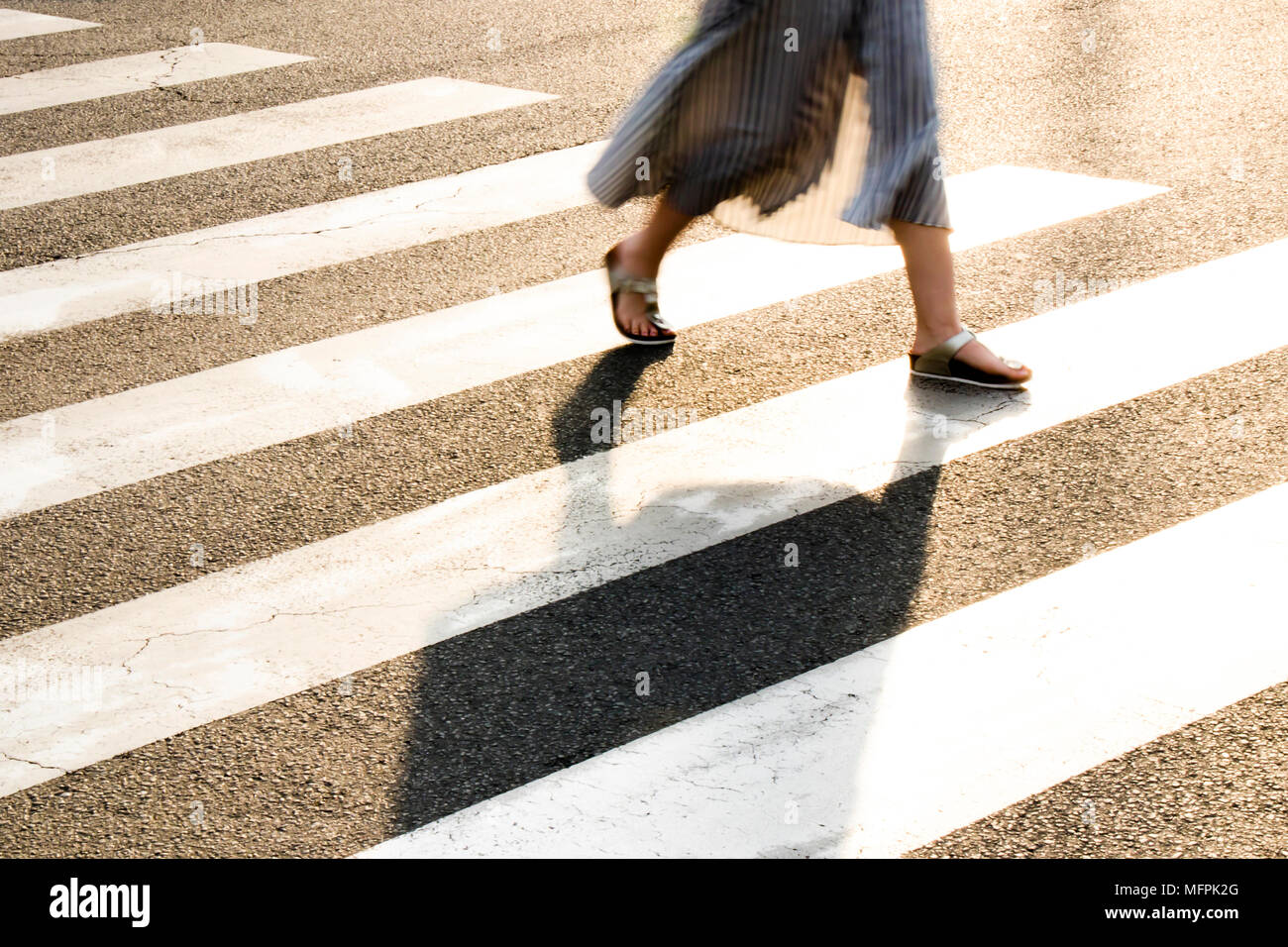 Beine einer jungen Frau im langen Kleid flattern im Sommer Brise während der Überquerung der Straße der Stadt im Sonnenuntergang Stockfoto