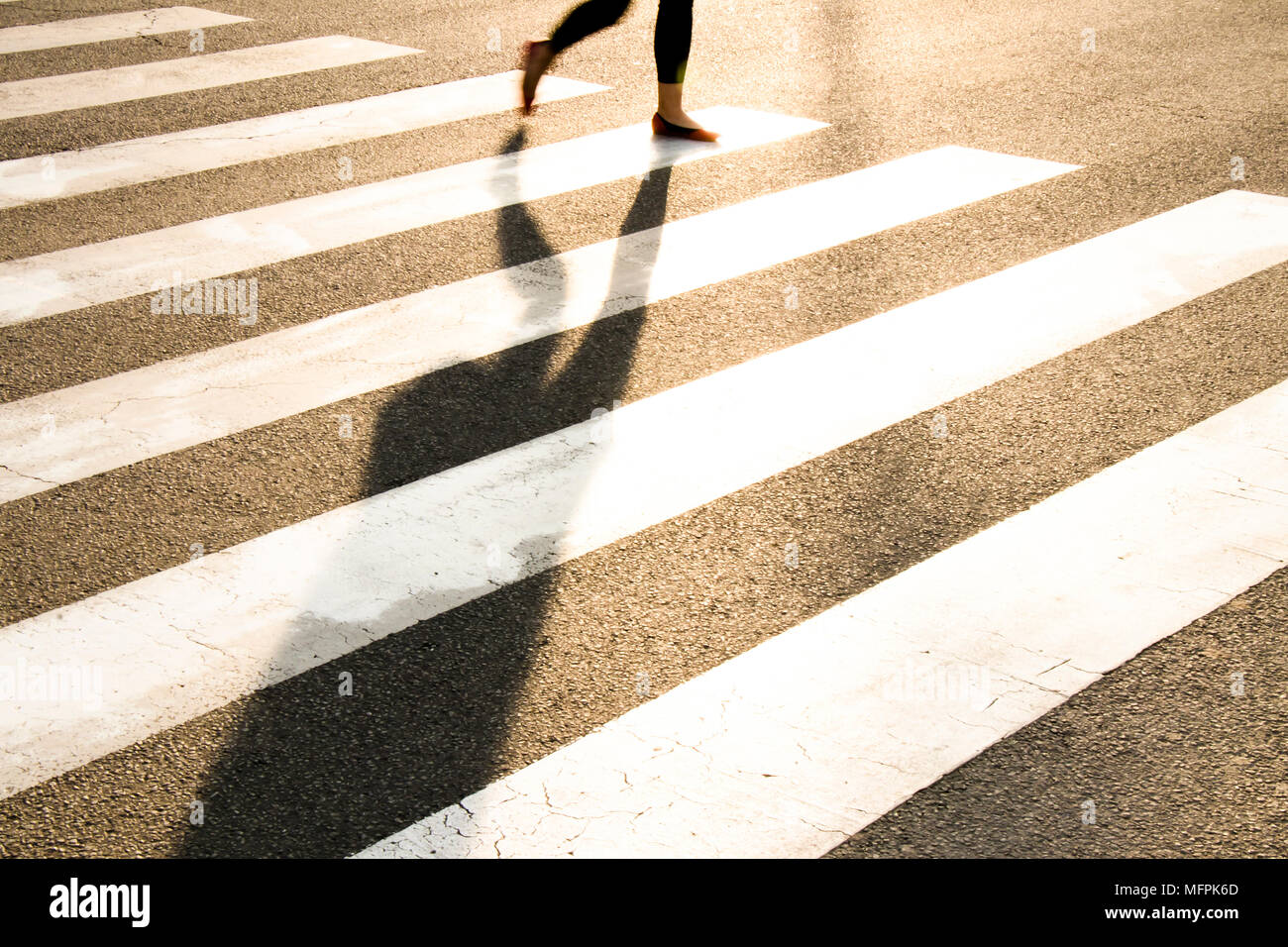 Stadt Straße Fußgängerüberweg mit den Beinen einer Frau zu Fuß in motion blur, lange Schatten im Frühjahr Sonnenuntergang Stockfoto