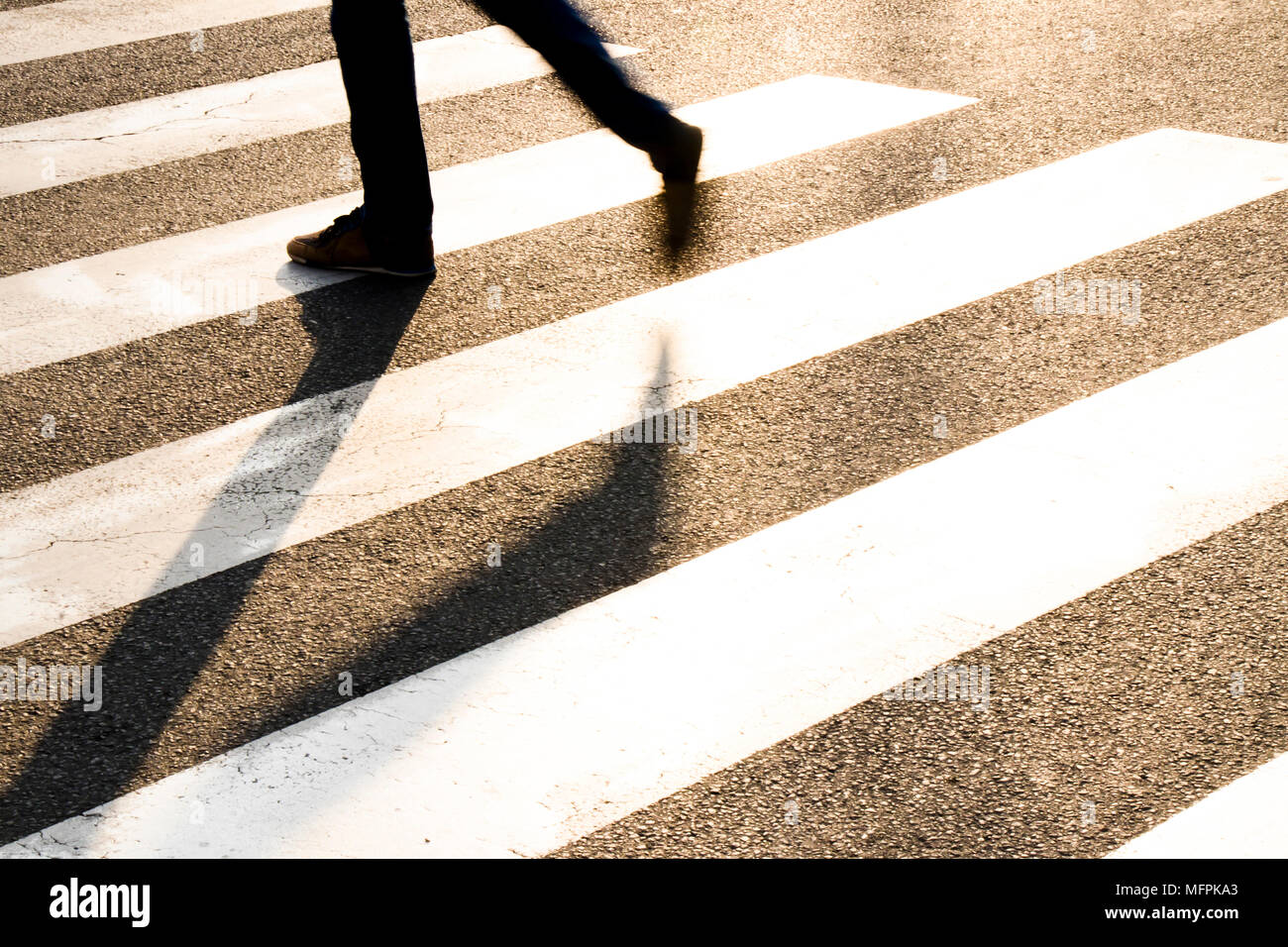 Stadt Straße Fußgängerüberweg mit Beine eines Mannes wandern in motion blur, lange Schatten im Sonnenuntergang Stockfoto