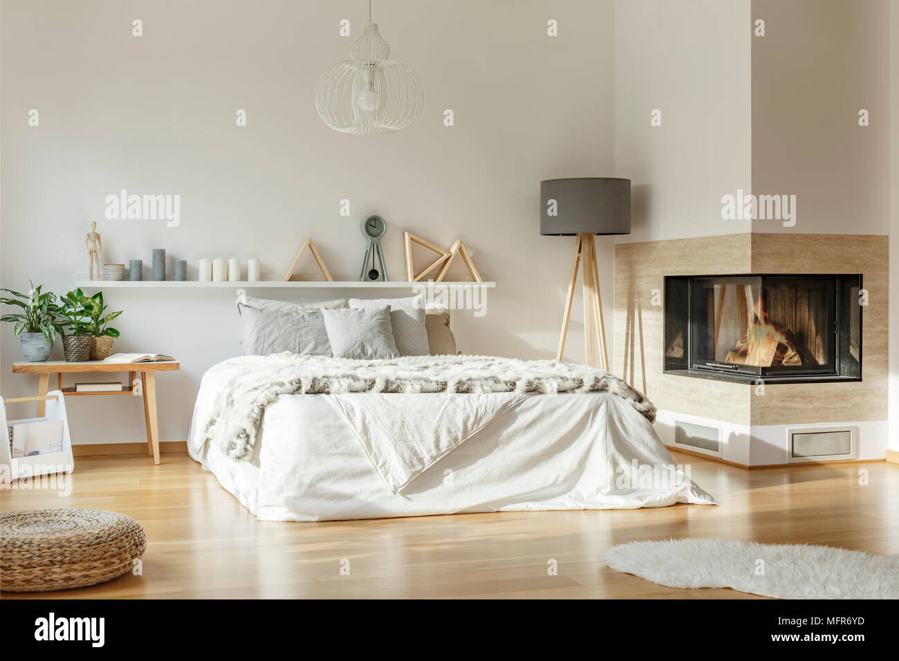 Geräumiges Schlafzimmer mit Kamin, großes Bett, Lampe, Wolldecke und Ornamente Stockfoto