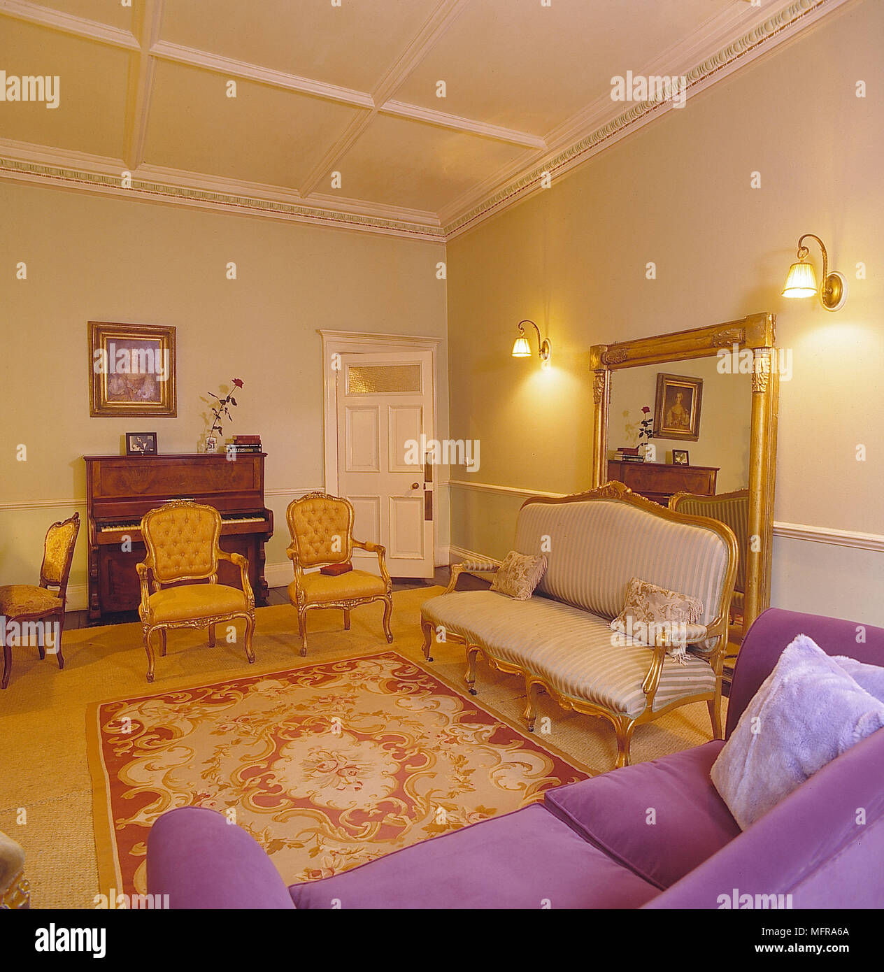 Wohnzimmer gelben Wänden roten Teppich goldenen Teppich lila Couch gold Stühle piano Große gold Spiegel Ineteriors zimmer Antiquitäten Gemälde Wandleuchten plasterw Stockfoto