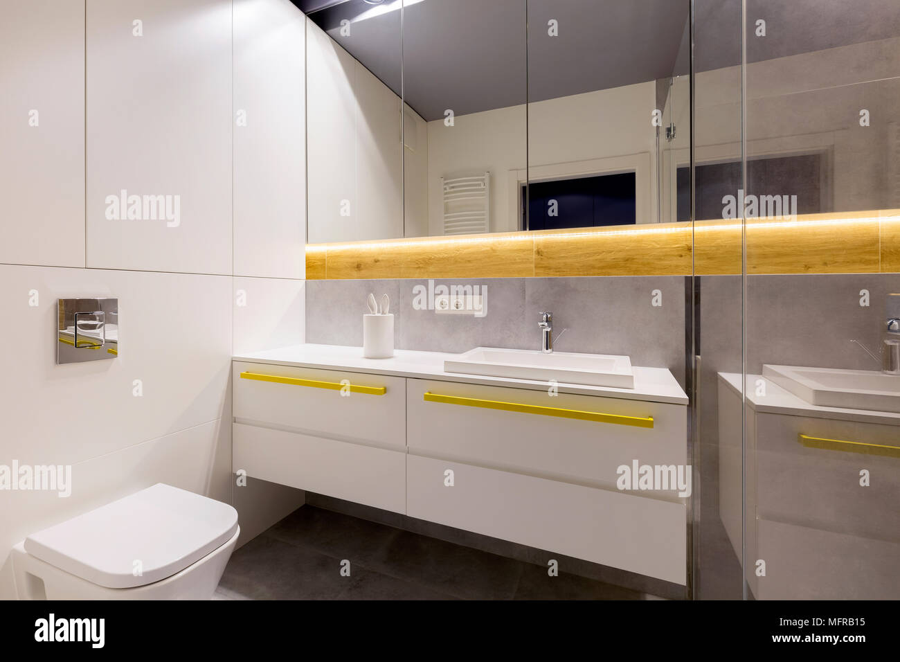 Sauberes, modernes Badezimmer mit Wc, Weißes Gehäuse, gelbe Griffe, Spiegel und grauen Fliesen Stockfoto