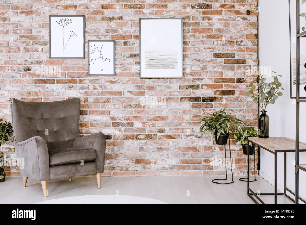 Wohnzimmer Einrichtung mit grauen Sessel, Pflanzen und Poster auf einem Red brick wall Stockfoto