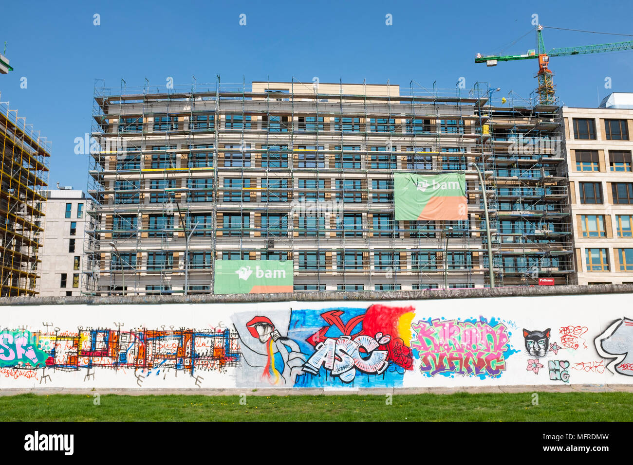 Blick auf den ursprünglichen Abschnitt der Berliner Mauer mit neuen Bürogebäude im Bau nach hinten an der East Side Gallery in Friedrichshain, Berlin, Deutschland. Stockfoto