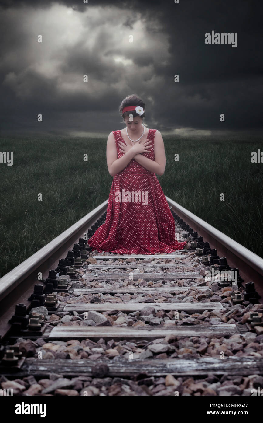eine Mädchen in einem roten Kleid sitzt auf Bahngleise Stockfoto