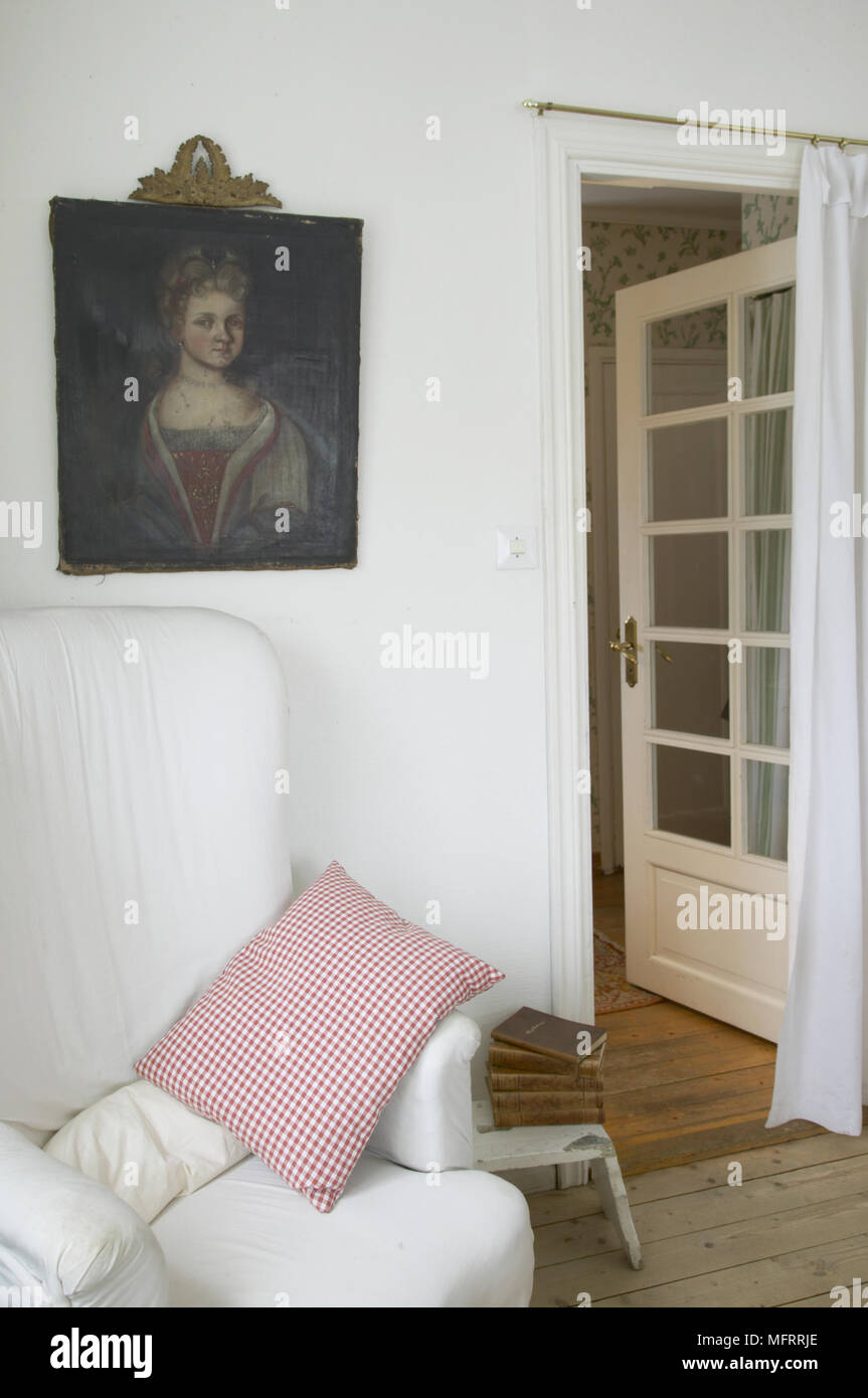 Traditionelle Wohnzimmer Detail mit offenen verglasten Tür Holz Fußboden und ein Portrait Malerei über einen gepolsterten Sessel und. Stockfoto