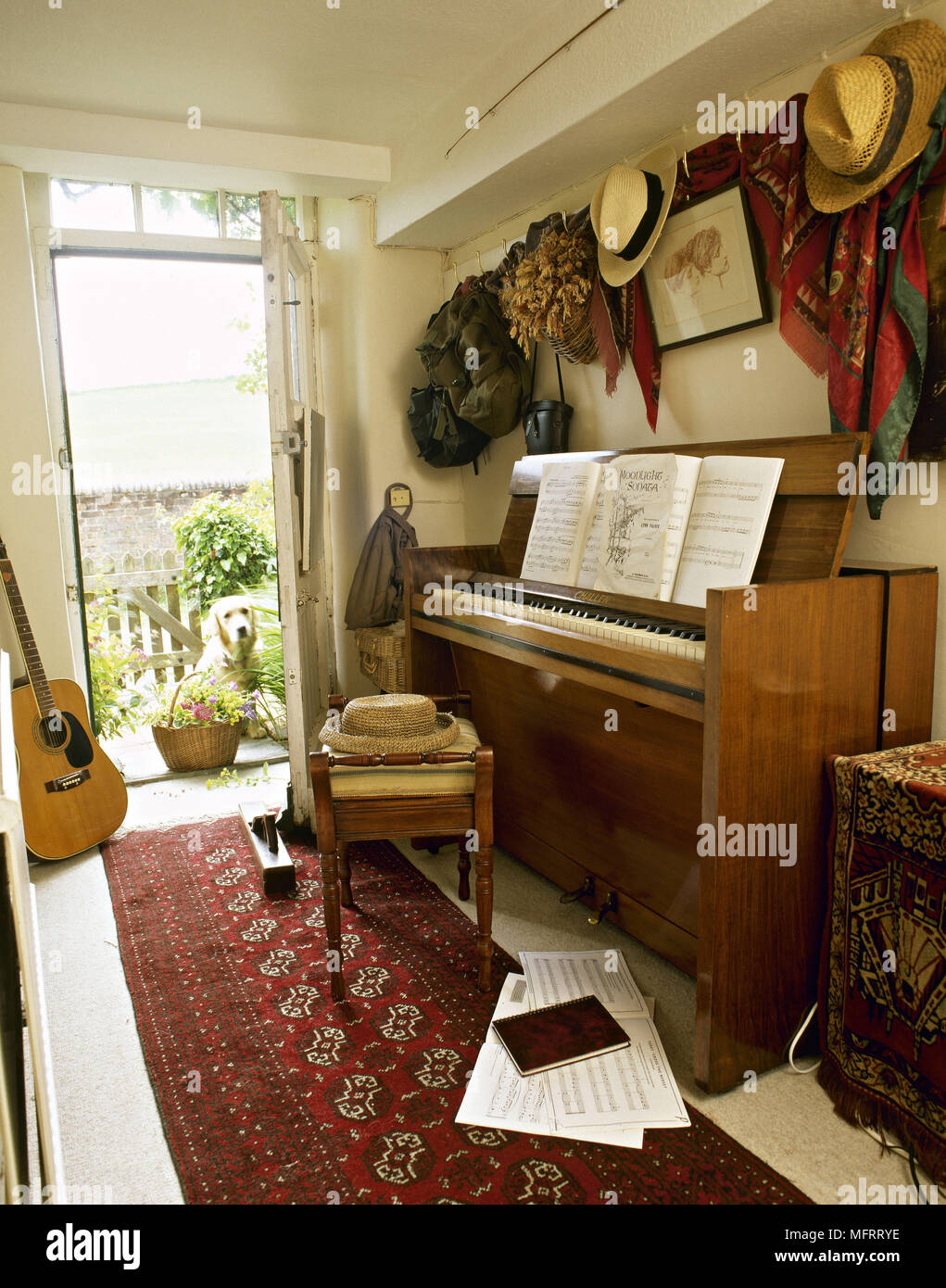 Land Flur mit Klavier Hocker Noten hängen Hüte und ein Hund suchen durch die offene Tür. Stockfoto