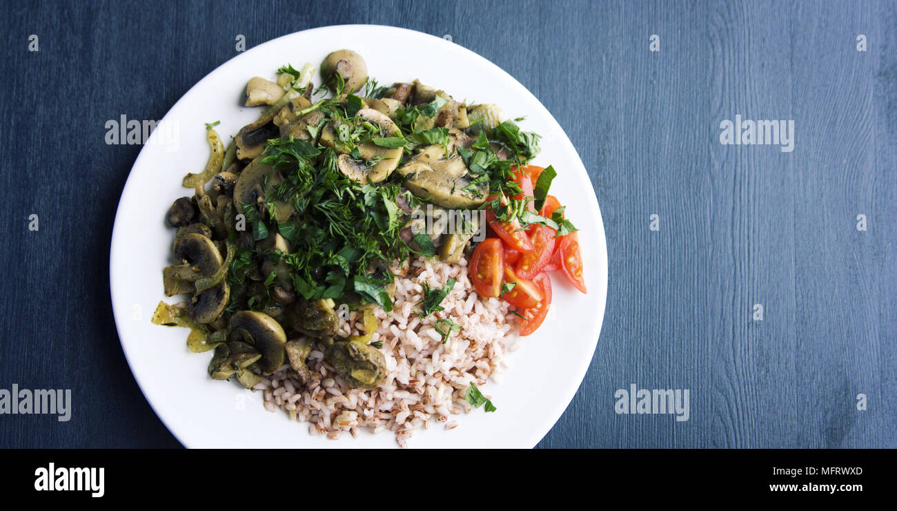 Roter Reis mit Pilzen und Tomaten. Vegane Gerichte. Europäische Küche. Einfach gesundes Mittagessen auf dem schwarzen Hintergrund. Vegetarisches Reisgericht auf dem w Stockfoto