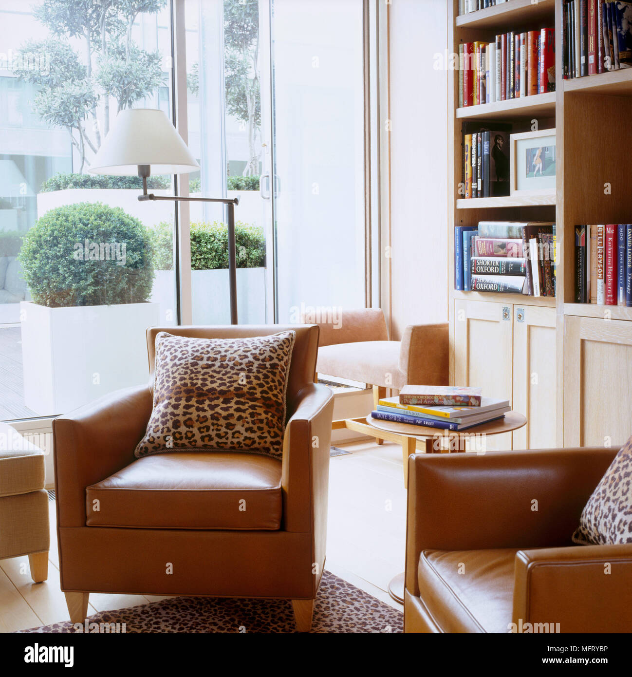 Ein modernes Wohnzimmer mit gelbbraunen Ledersesseln Bücherregal runde Seite Tabelle Stehleuchte Leopardenfell Polster drucken Stockfoto