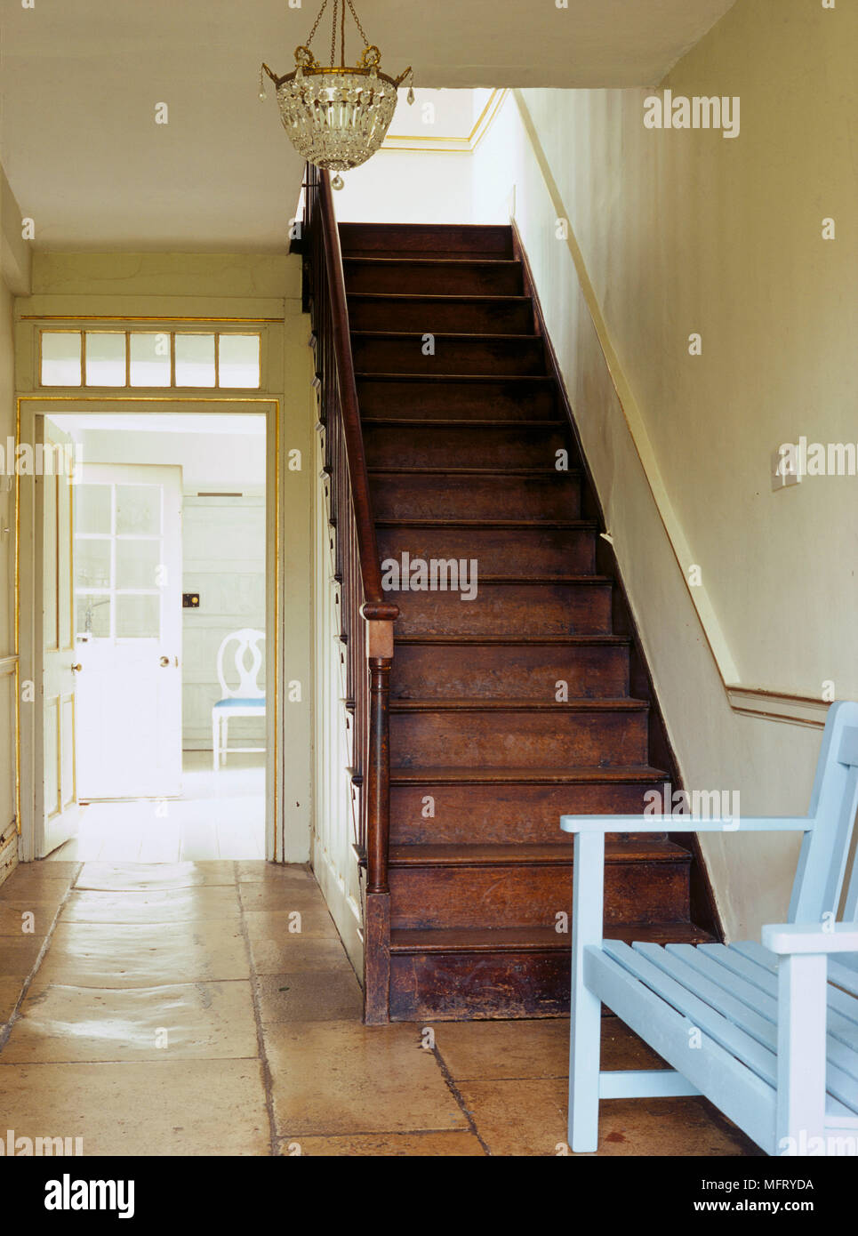Eine Traditionelle, in neutralen Flur mit Steinplatten Boden und Holztreppe mit Blick durch die offene Tür hinaus Stockfoto