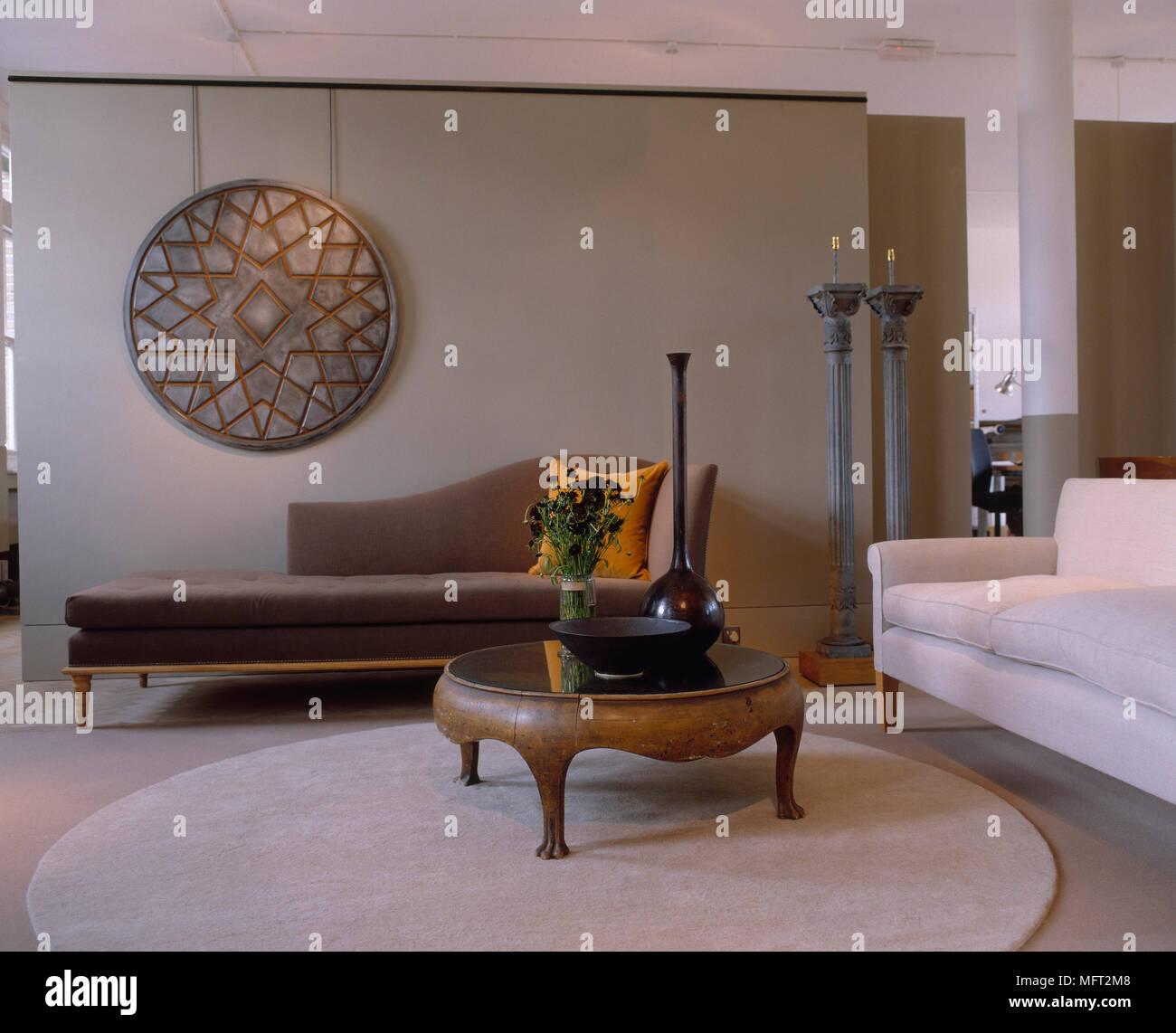 Modernes Wohnzimmer Mit Einem Braunen Chaiselongue Weissen Sofa Runden Holzernen Couchtisch Kunstwerke Und Eine Gespiegelte Spalte Stockfotografie Alamy