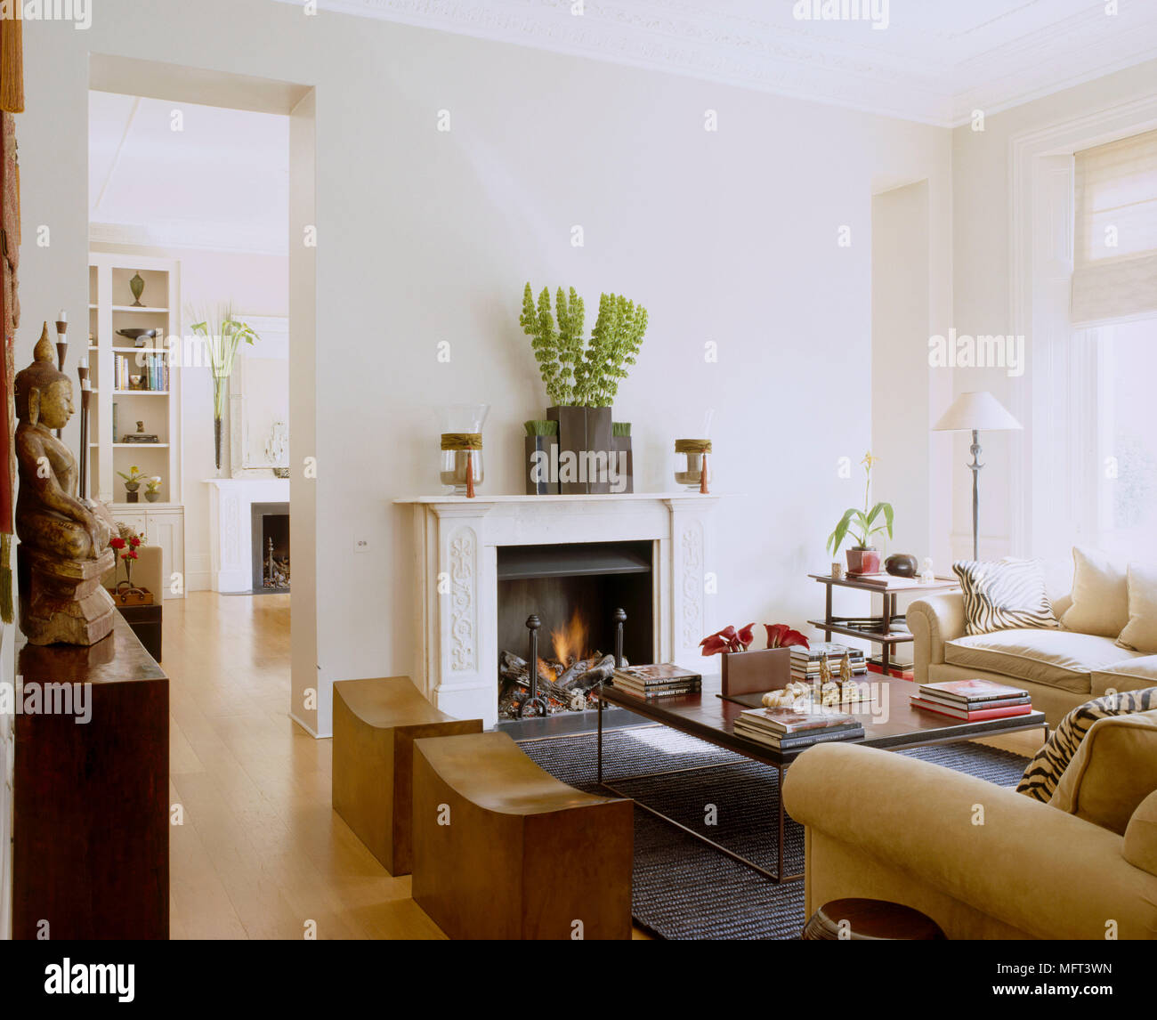 Eine Traditionelle, in neutralen Wohnzimmer Kamin mit Feuer angezündet gepolstertes Sofa Holz Couchtisch Blick durch die offene Tür zu Raum jenseits Stockfoto