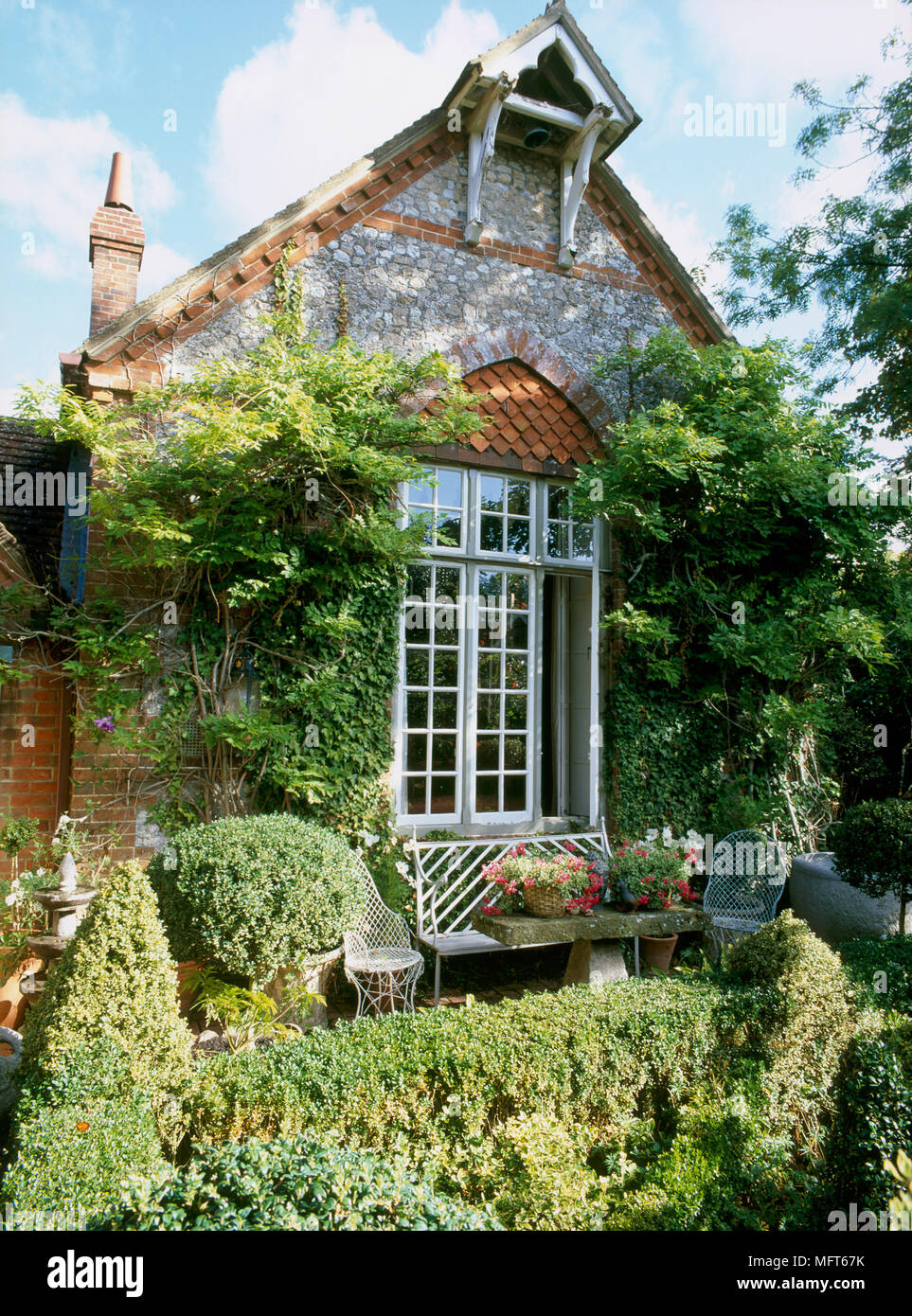 Eine Außenansicht von einem Stein und Ziegel Land, Haus und Garten, gewölbte Kacheln über dem Fenster, Terrasse umgeben von Hedging, Steinbank Stockfoto