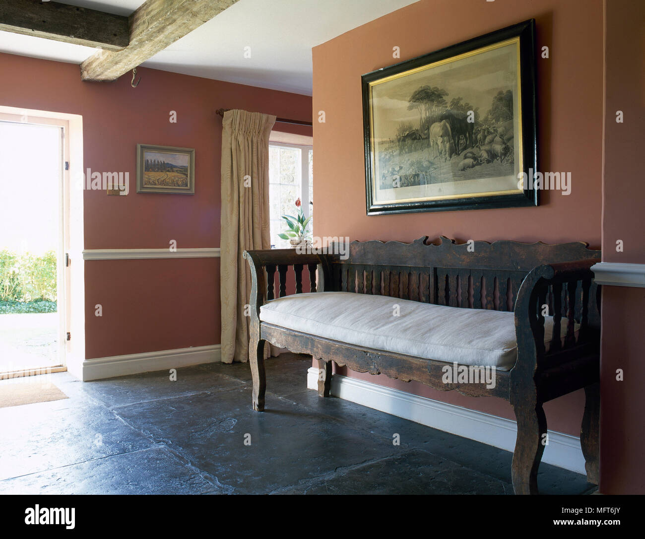 Landhaus Eingangsbereich mit Terracotta Farbe Wände, Decke mit Holzbalken, Steinplatte, und eine antike, gepolsterte Sitzbank. Stockfoto