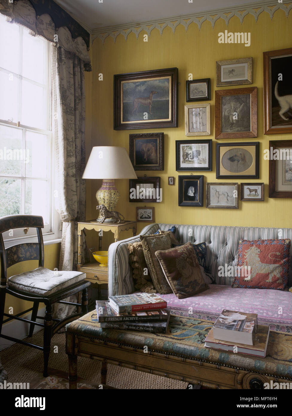 Ein traditionelles gelb Wohnzimmer mit gemalten Fries gepolstertes Sofa osmanischen Seite Tischleuchte Sammlung von Gemälden Stockfoto