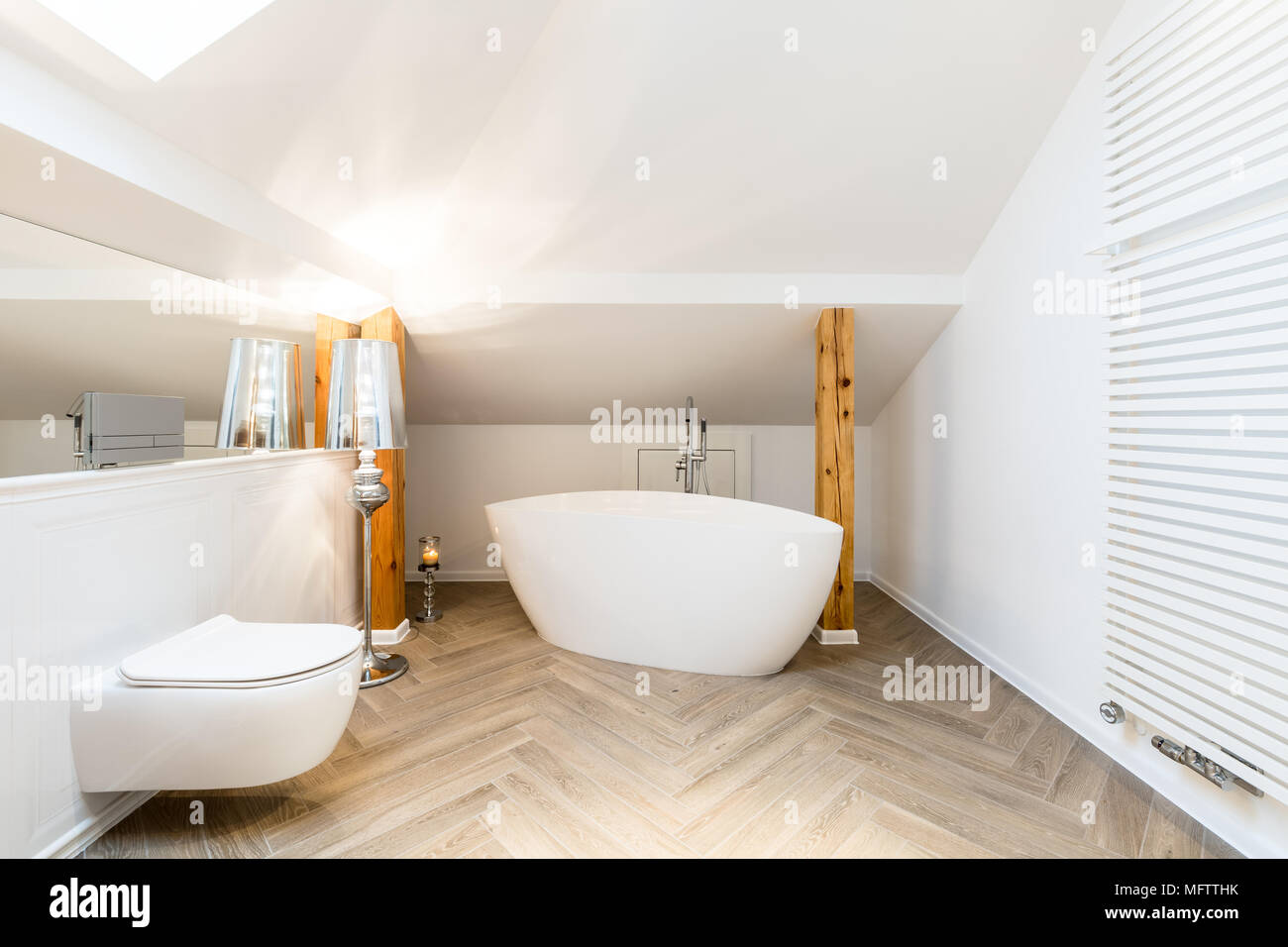 Modernes, weißes Bad im Dachgeschoss mit ovalen, keramische Wanne, Wandheizung und Holzbalken Stockfoto