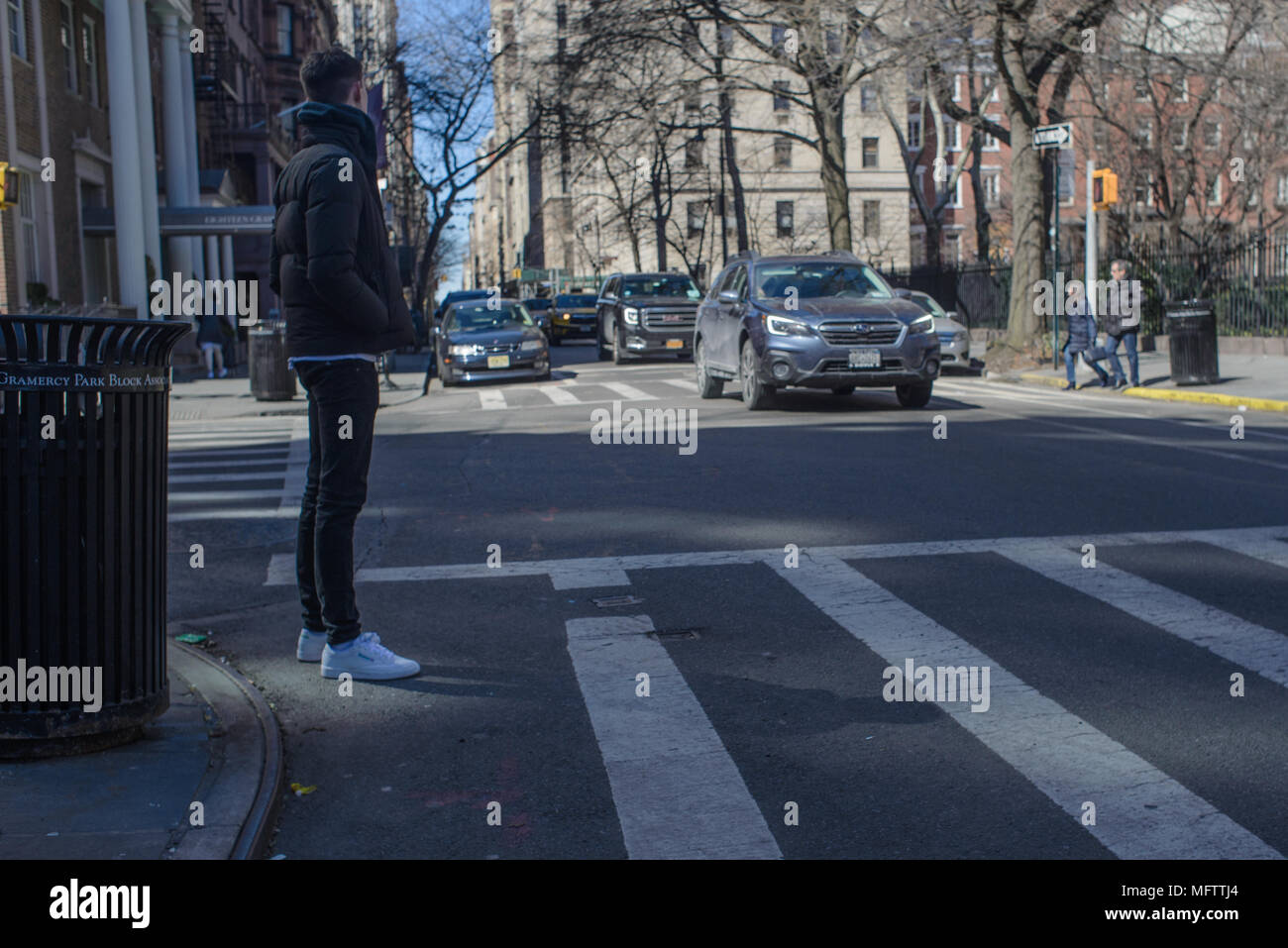 Ein junger Mann im weißen Turnschuhen wartet im Schatten der Straße in Gramercy Park an einem sonnigen Frühlingsmorgen zu überqueren. Stockfoto