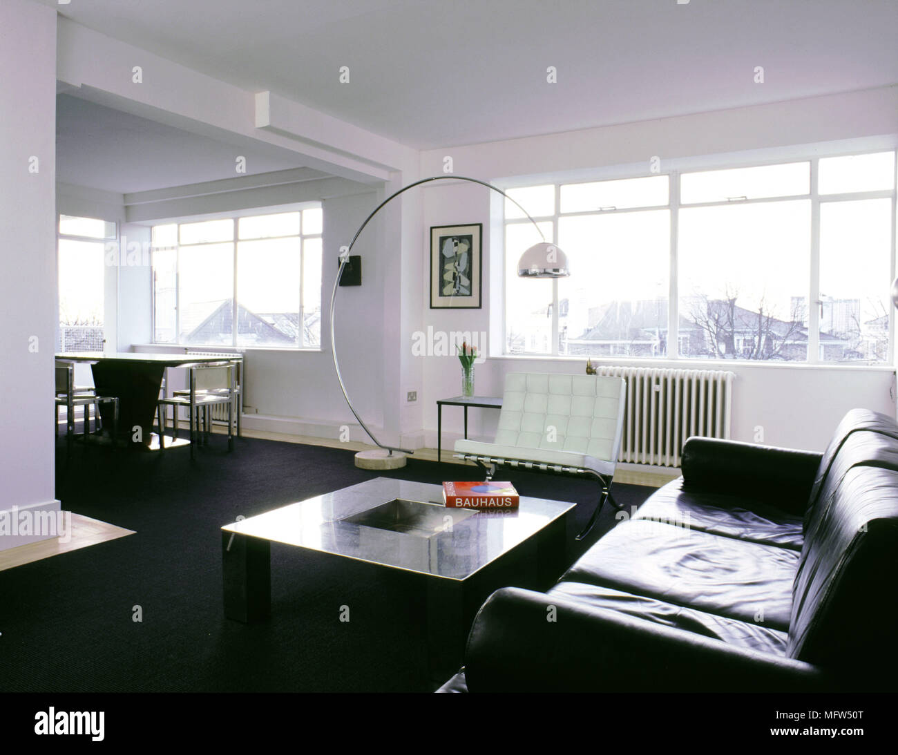 Moderner, offener Wohnbereich mit schwarzer Teppich Esstisch und Stühle leder Sofa geschwungene Stehleuchte und sonnigen Fenster. Stockfoto