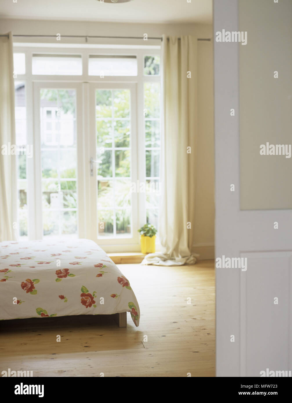 Ein Detail der ein modernes Schlafzimmer in neutralen Farben Doppelbett mit Blumenmuster Abdeckung Holz, französischen Fenstern Vorhänge obwohl offene Tür gesehen Stockfoto