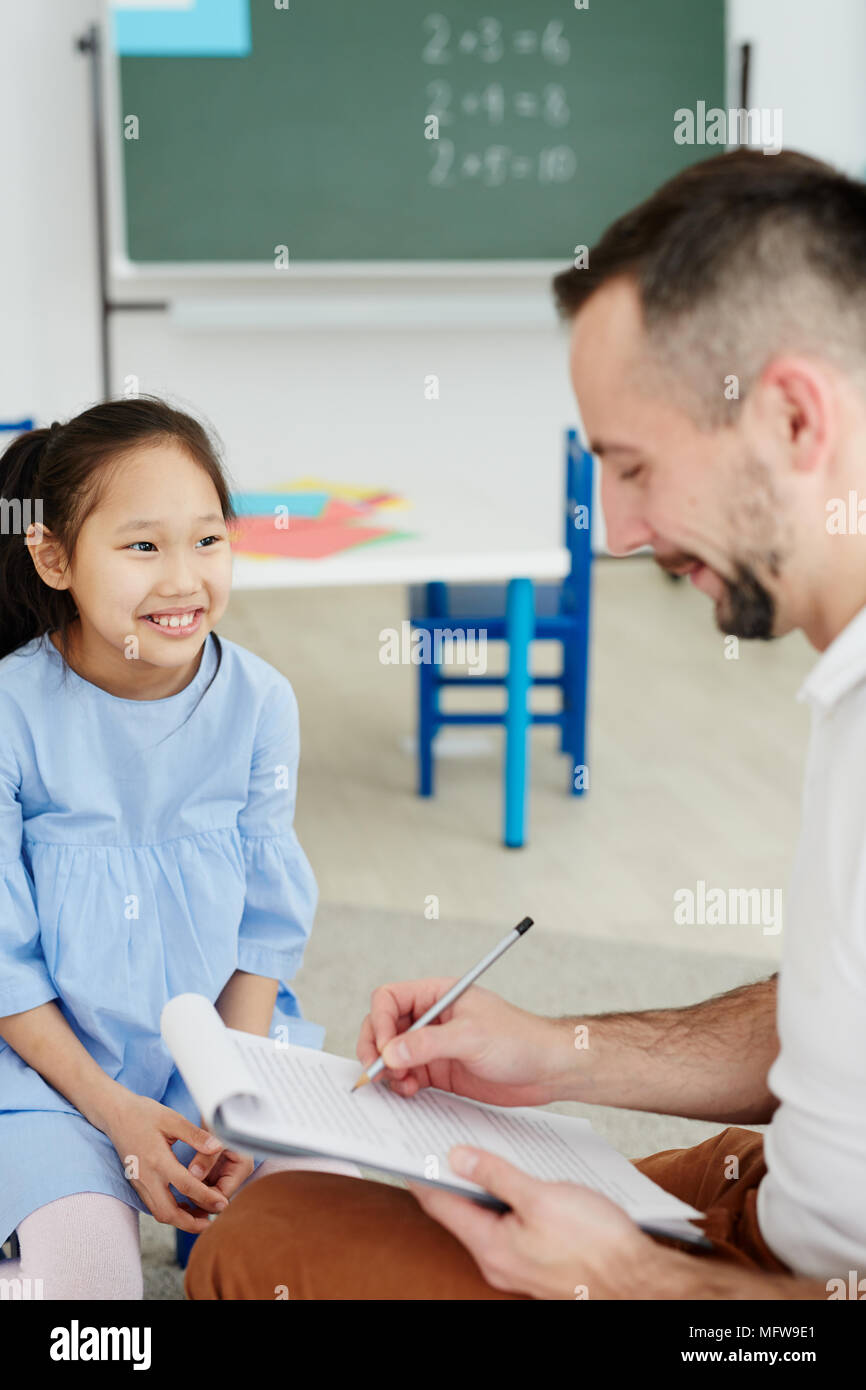 Männliche Lehrer etwas schreiben über die Zwischenablage, während Sie eine privatstunde asiatischen Mädchen neben ihm saß zu fröhlichen Stockfoto