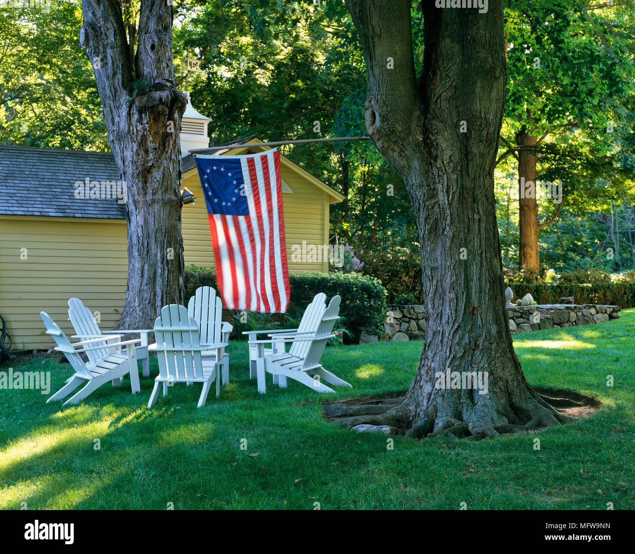 Adirondack Stühle im Garten unter Bäumen mit amerikanischer Flagge Stockfoto