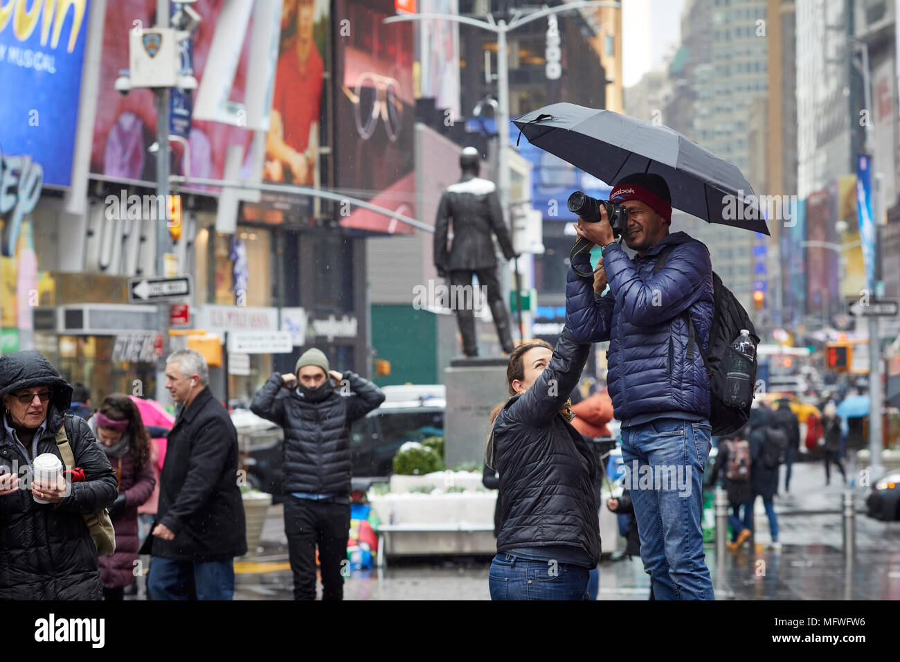 Manhattan in New York City Tourist nimmt ein Bild mit seiner Kamera im Times Square Wahrzeichen als Freund Tierheim hilft mit einem Regenschirm Stockfoto