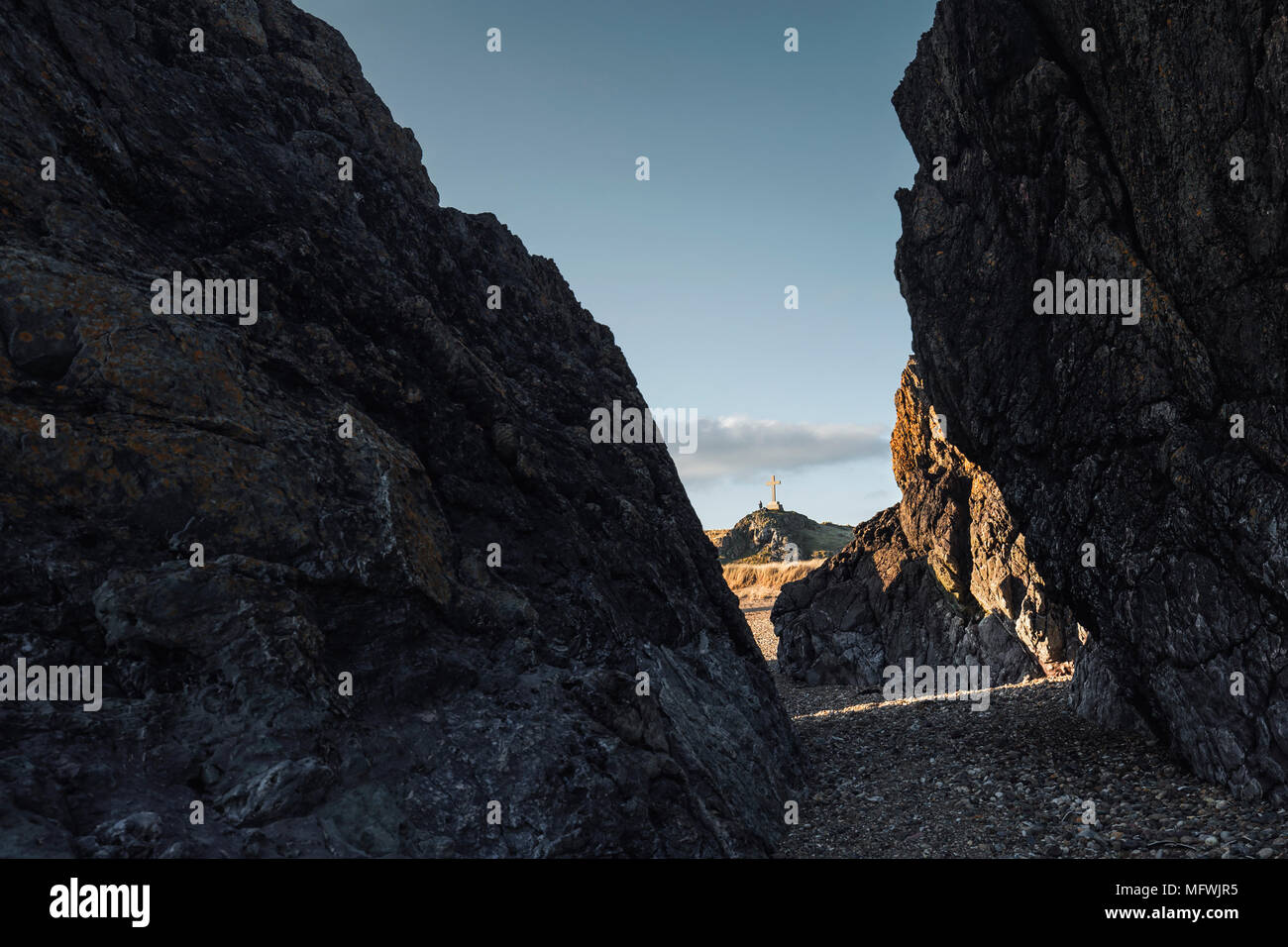 Llandwyn Insel kreuz Monument sehen durch Felsen bei Ebbe. Ynys Llanddwyn in Nord Wales, Großbritannien Stockfoto