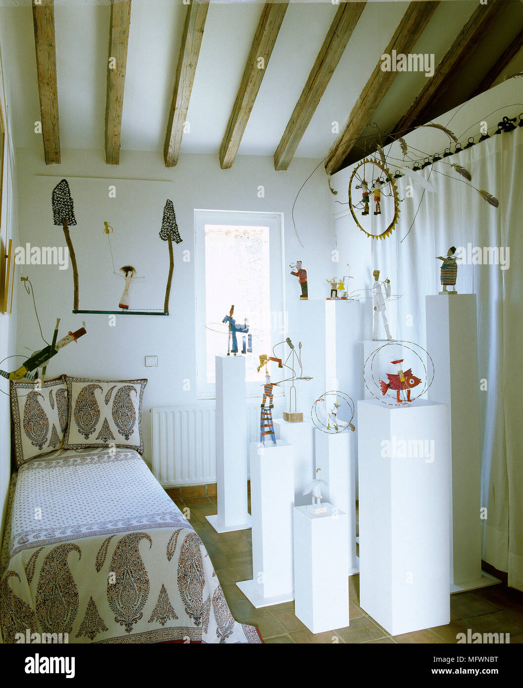 Künstlerische Schlafzimmer mit Holzbalkendecke, Doppelbett mit Grafik Bettdecke und eine Sammlung von Skulpturen auf Sockeln. Stockfoto