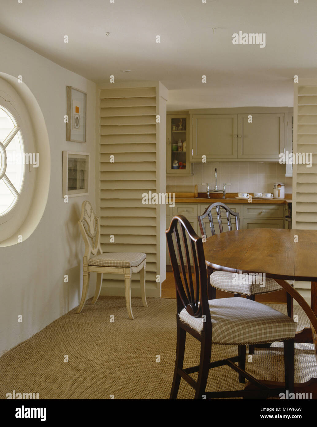 Esszimmer mit rundem Fenster mit Tisch und Stühlen vor der Küche mit Holztäfelung Stockfoto