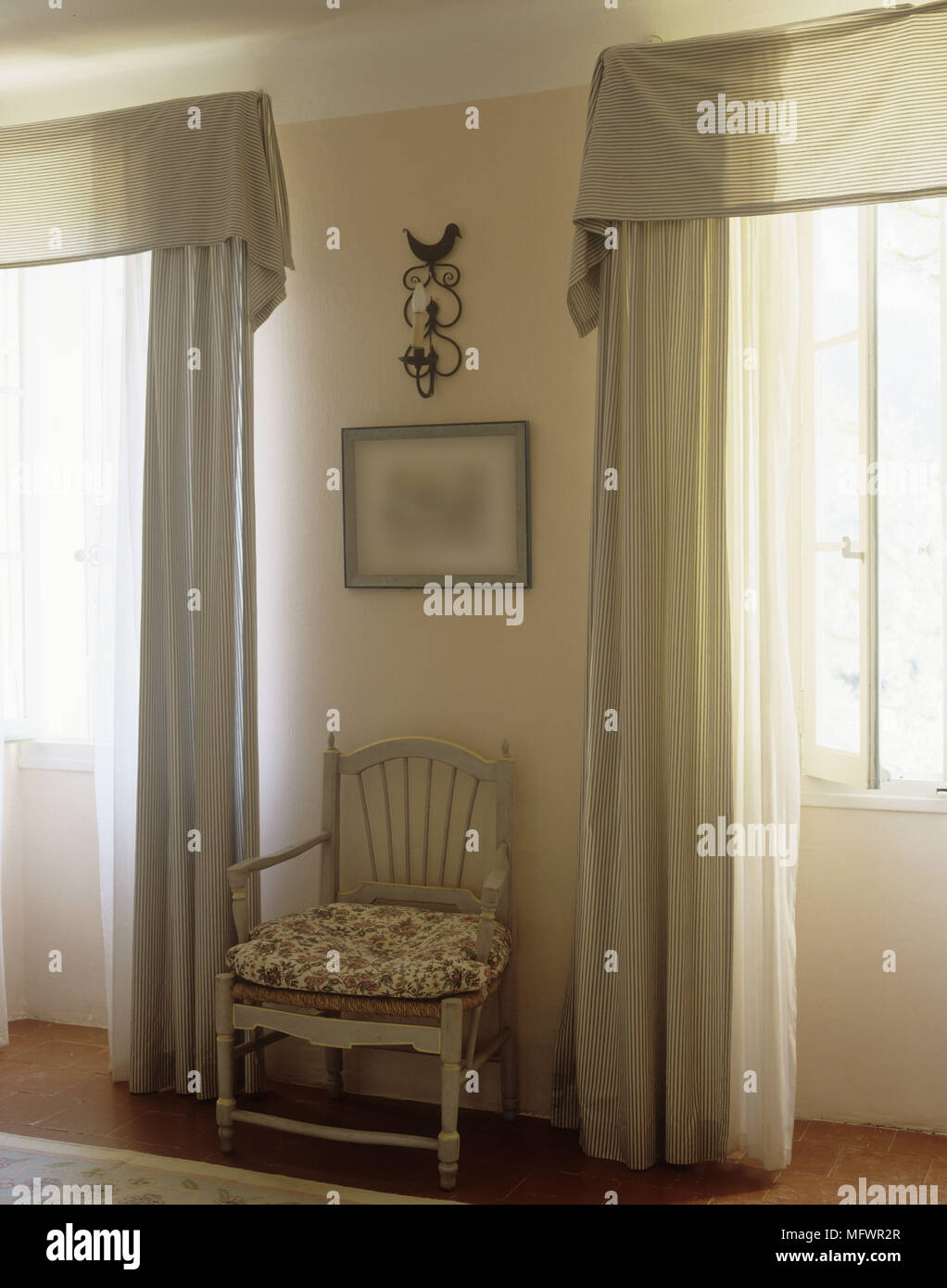 Stuhl zwischen zwei Fenster mit langen Vorhängen Stockfoto