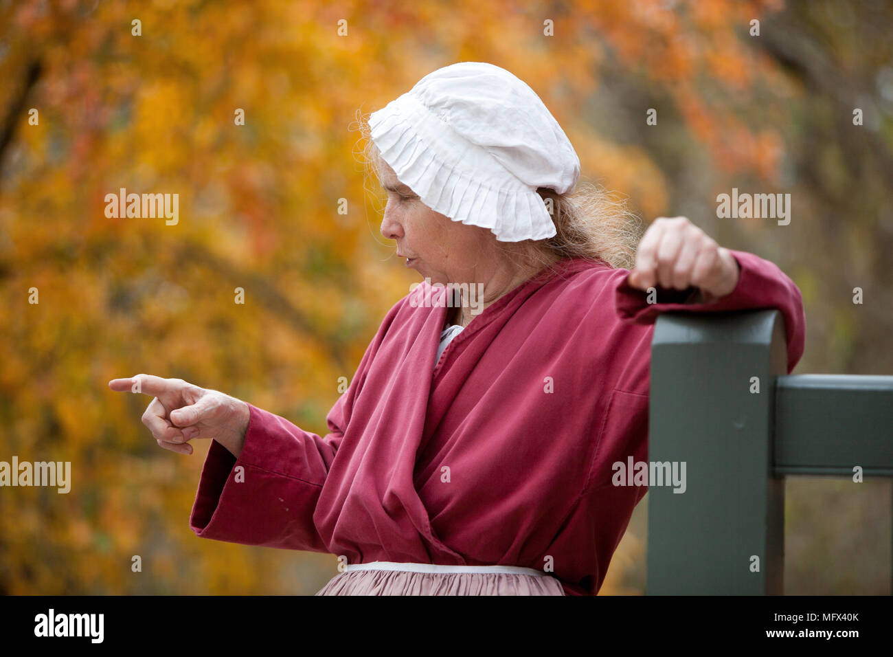 Porträt einer Frau, die in der frühen amerikanischen Kleid tragen eines traditionellen Motorhaube in Colonial Williamsburg Virginia Lattenzaun im Vordergrund. Stockfoto