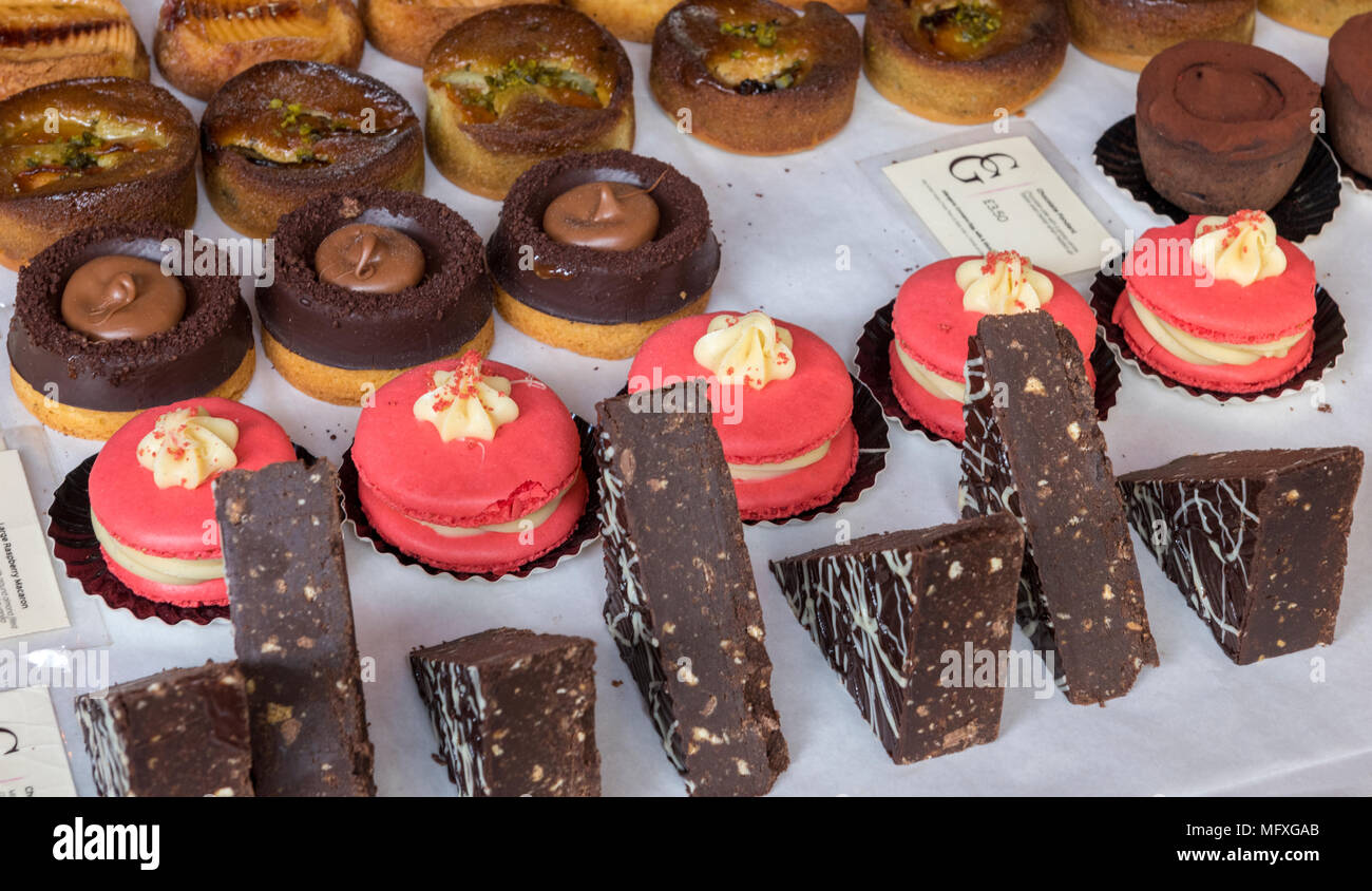 Eine Auswahl an leckeren süßen Leckereien und Kuchen ausgefallenen Dekorationen und Sahnehäubchen auf einem Stall in einem feinkostgeschäft oder Konditoren Londons am Borough Market. Stockfoto