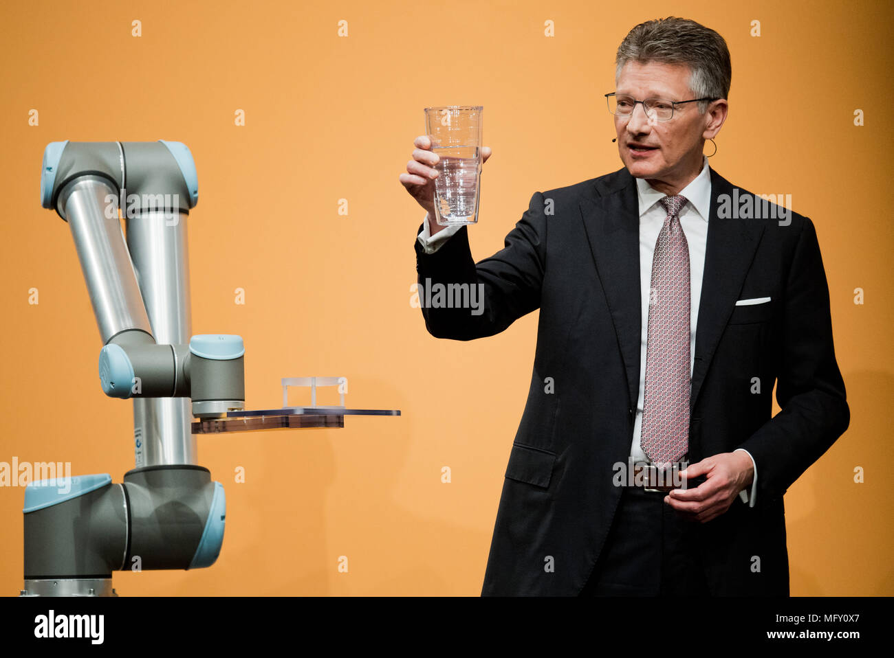 27 April 2018, Deutschland, Hannover: Elmar Degenhart, Vorstandsvorsitzender der Continental AG, mit einem Glas zur Hälfte mit Wasser gefüllt, neben einem Cobot Roboter, die in der kontinentalen Fabriken in der Mensch-roboter-cooperationg bereitgestellt werden, an der Continental AG Hauptversammlung im Hannover Congress Centrum (HCC). Foto: Julian Stratenschulte/dpa Stockfoto
