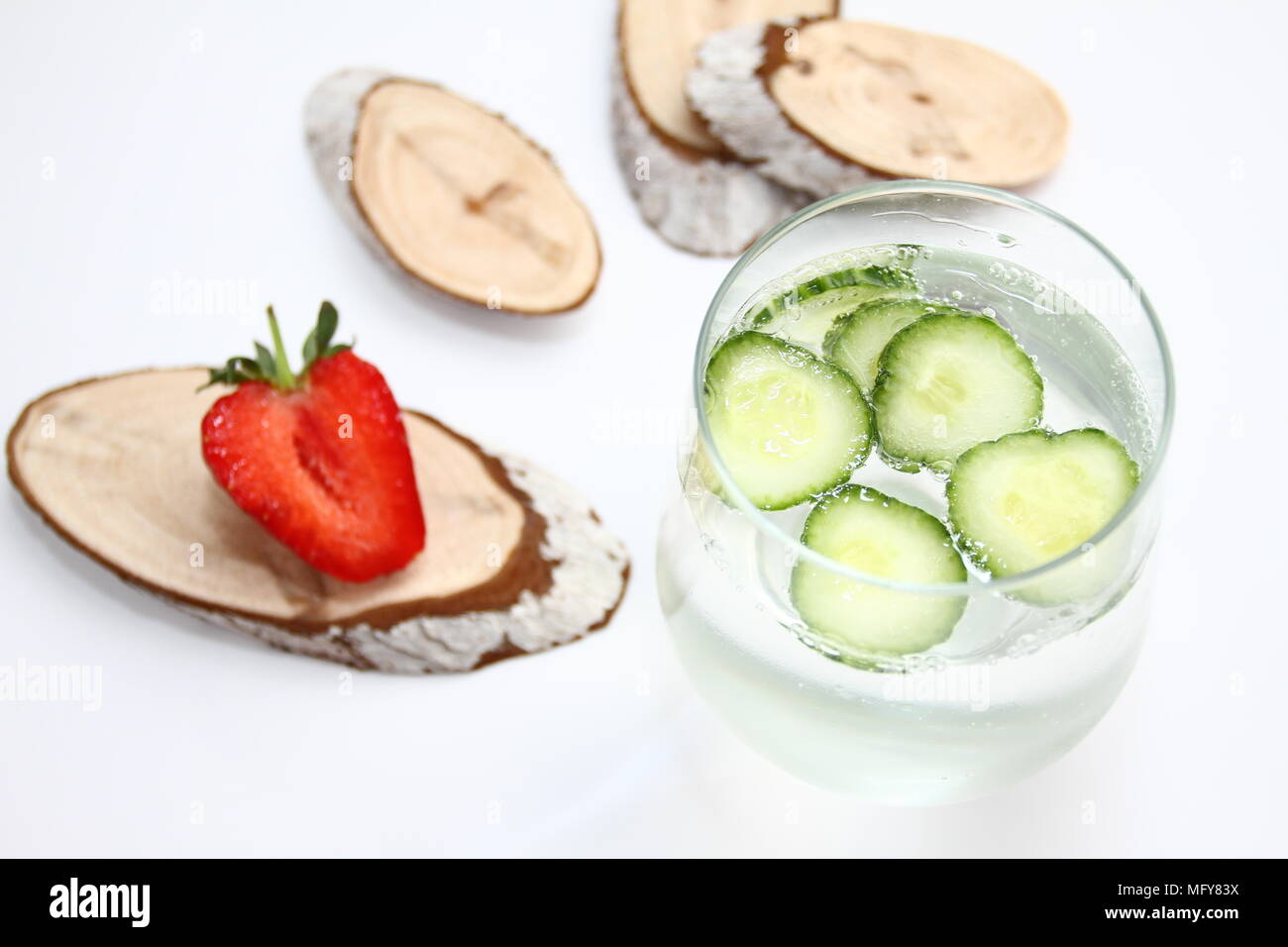 Detox aromatisiertes Wasser mit Gurke auf weißem Hintergrund mit roten Erdbeere und Holz Dekoration. Gesunde Ernährung Konzept. Anti stress Trinken Stockfoto