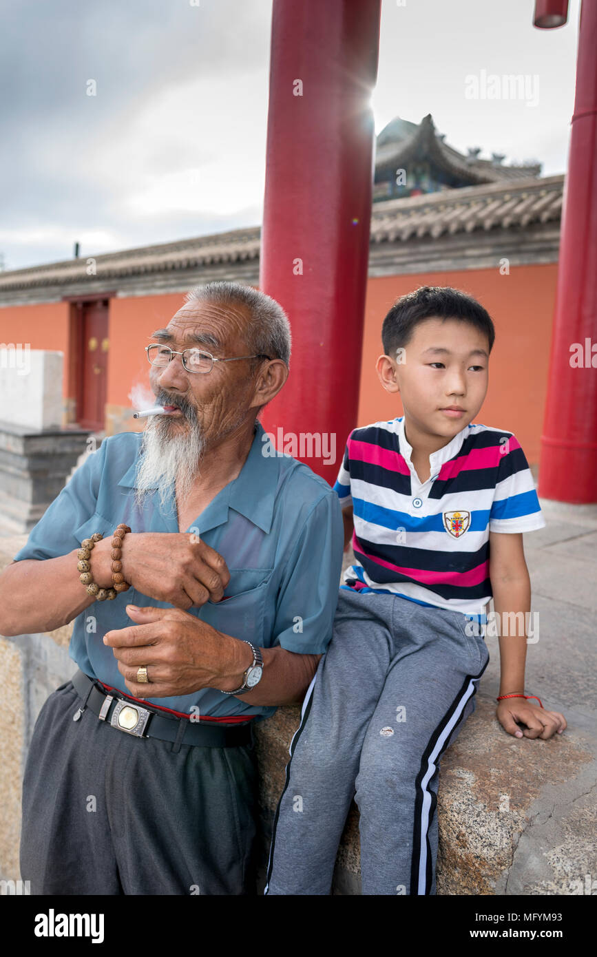 Großvater und Enkel rauchen Zigarette genießen Sie jeder des anderen Firma als Sonne über City Park auf Obo Hill, Xilinhot, Innere M Stockfoto
