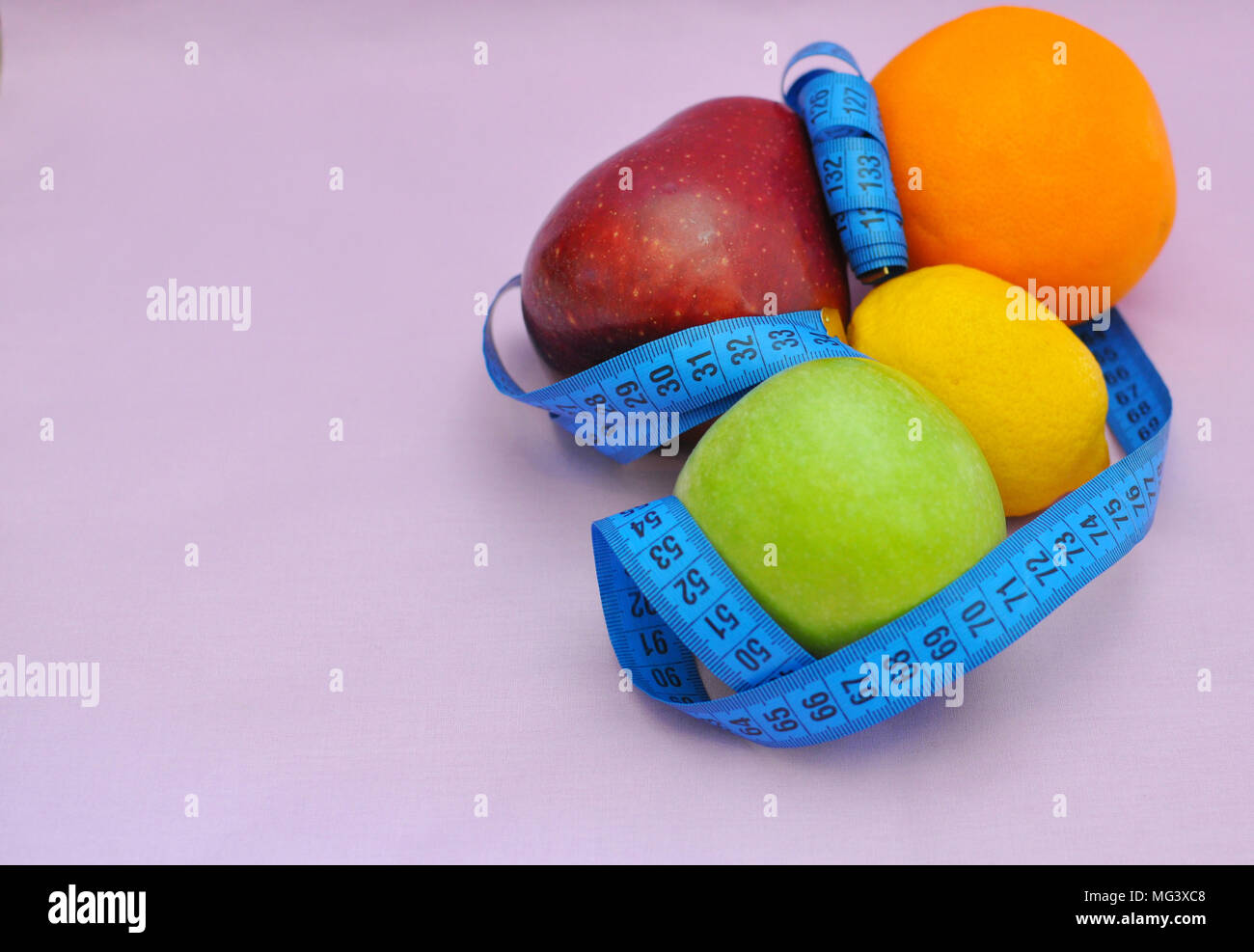 Äpfel, Zitrone und Orange mit einem blauen Tailoring meter auf rosa Hintergrund, Oberseite, closeup gewickelt Stockfoto