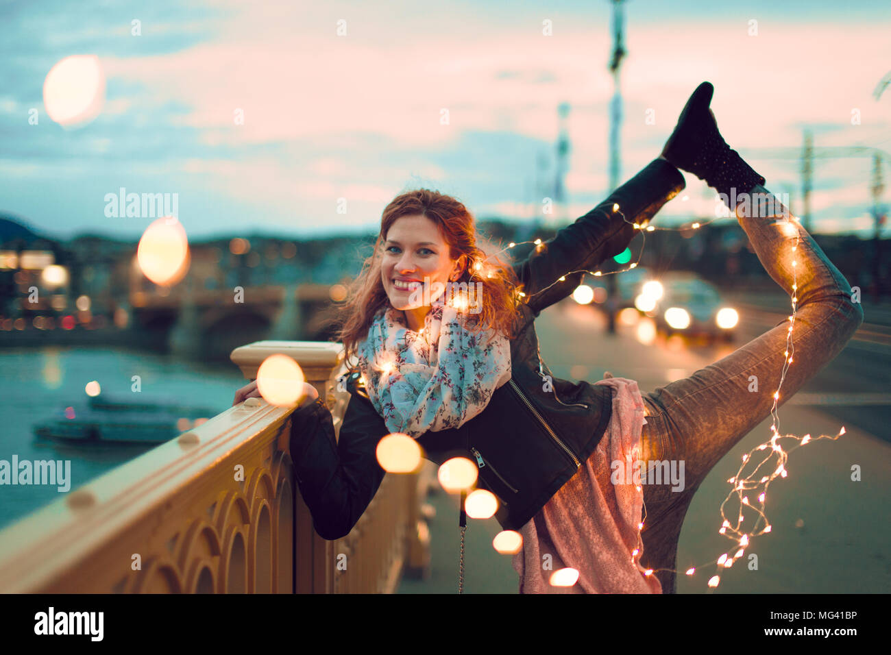 Glückliche junge rothaarige Frau Yoga mit Lichterketten im Freien und Lächeln, Blaugrün und Orange Style Stockfoto