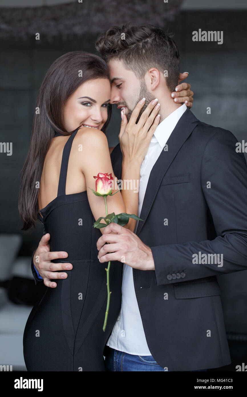 Glückliche junge stilvollen Mann mit Rose holding Arme schöne Frau in Innenräumen, Liebe Stockfoto