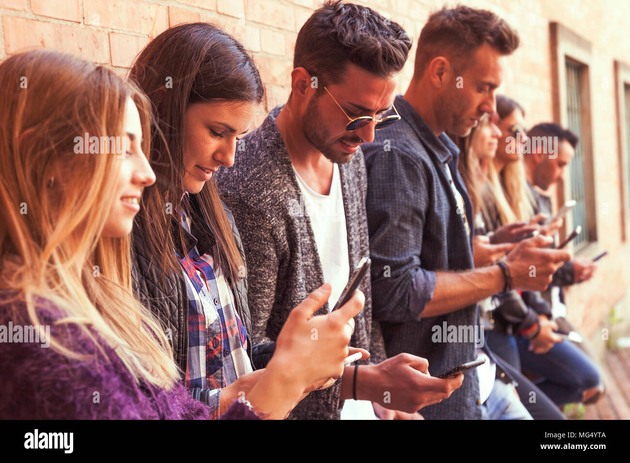 Große Gruppe von Freunden über Smart Phone gegen eine Rote Wand aus Ziegel - junge Menschen durch Mobile Smartphone süchtig-Technologie millennials Konzept Stockfoto